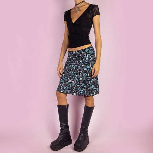 The Y2K Black Floral Mini Skirt is a vintage 2000s piece featuring a playful floral print in black and blue, with an elastic waist. It has a flattering high-waisted A-line silhouette, making it perfect for summer days or casual outings.