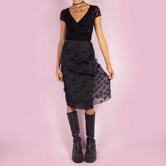 The Y2K Black Applique Midi Skirt is a vintage 2000s piece featuring intricate appliqué details throughout. This elegant skirt has a side zipper closure and a flattering high-waisted fit. It is semi-sheer, making it perfect for special occasions.