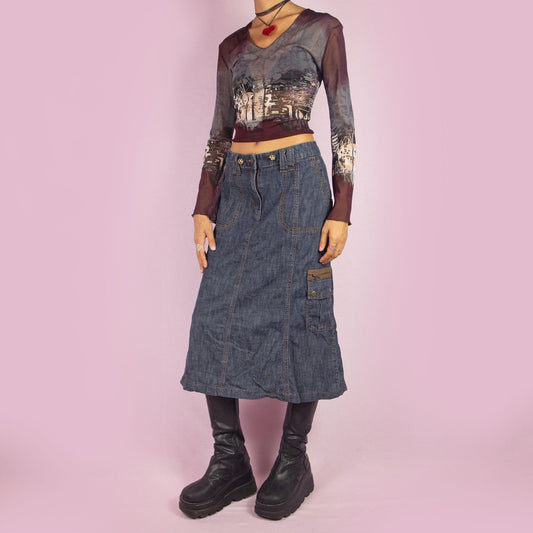 The Y2K Denim Cargo Midi Skirt is a vintage 2000s piece featuring a mid-rise silhouette, pockets, a side cargo pocket, and a front zipper closure. Perfect for casual outfits and everyday wear.