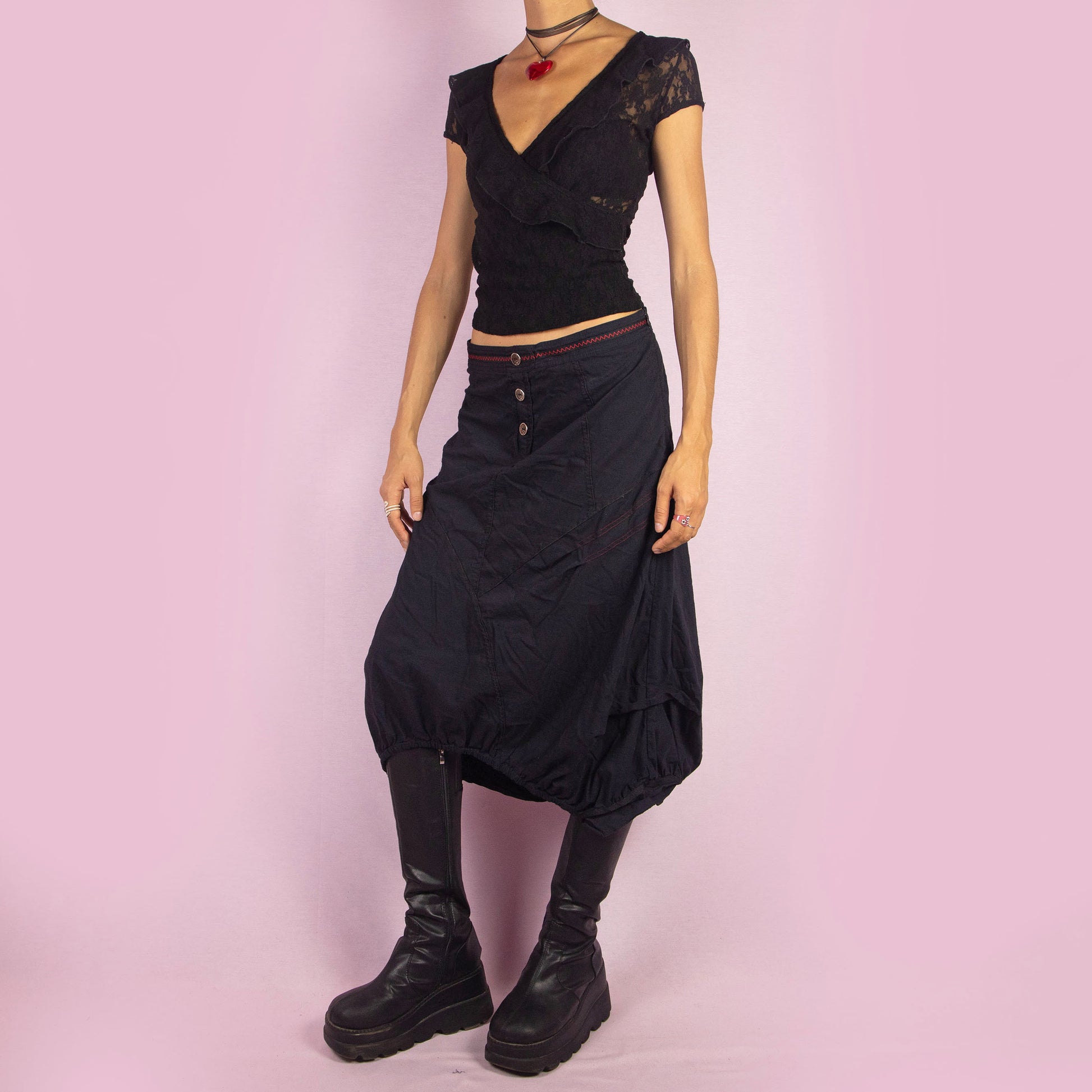 The Y2K Black Midi Balloon Skirt is a vintage 2000s piece featuring a button-front detail, stretchy fabric, and a side zipper closure. It includes pockets and has an avant-garde silhouette with a gathered hem, creating a balloon-style effect. Perfect for adding an edgy touch to casual outfits.