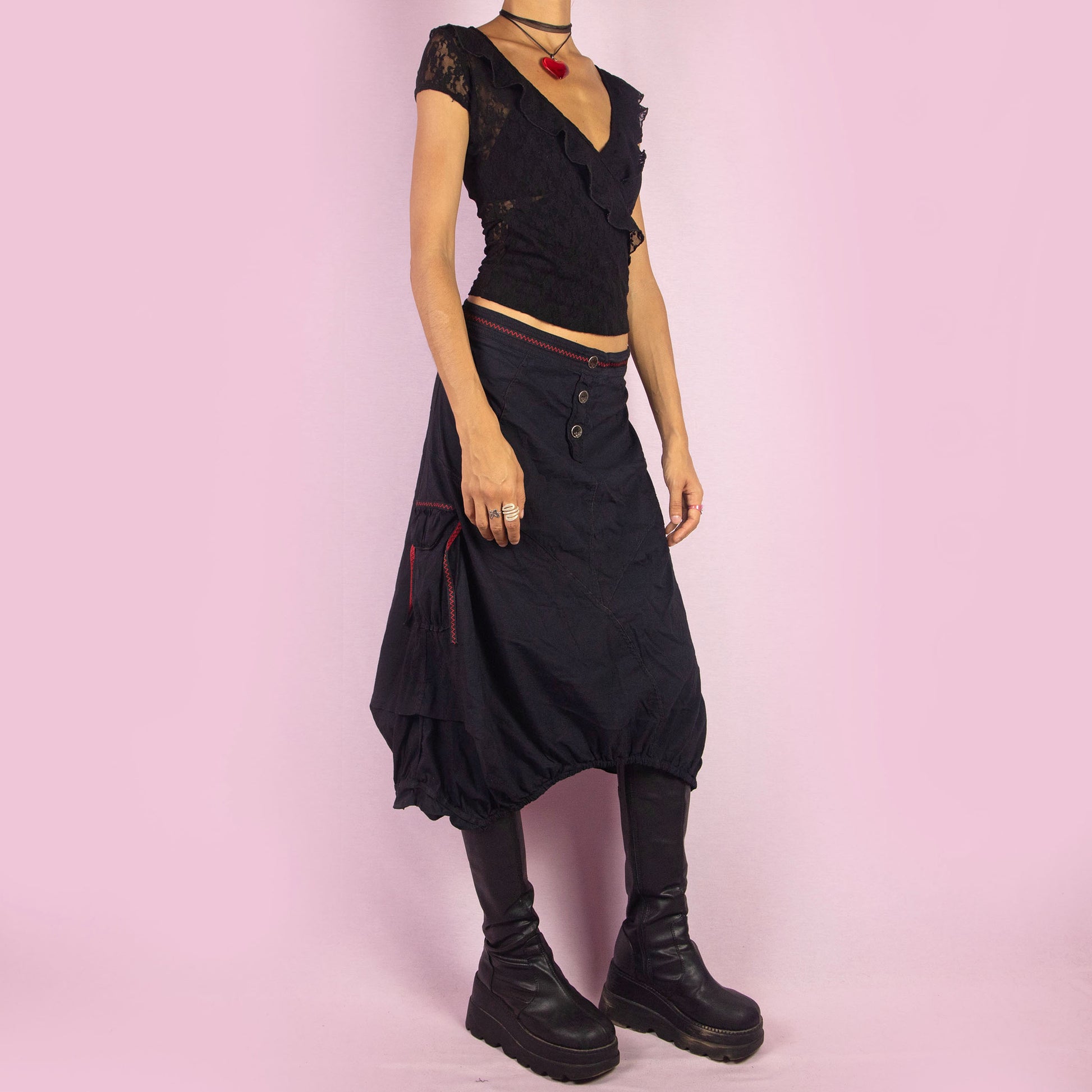 The Y2K Black Midi Balloon Skirt is a vintage 2000s piece featuring a button-front detail, stretchy fabric, and a side zipper closure. It includes pockets and has an avant-garde silhouette with a gathered hem, creating a balloon-style effect. Perfect for adding an edgy touch to casual outfits.