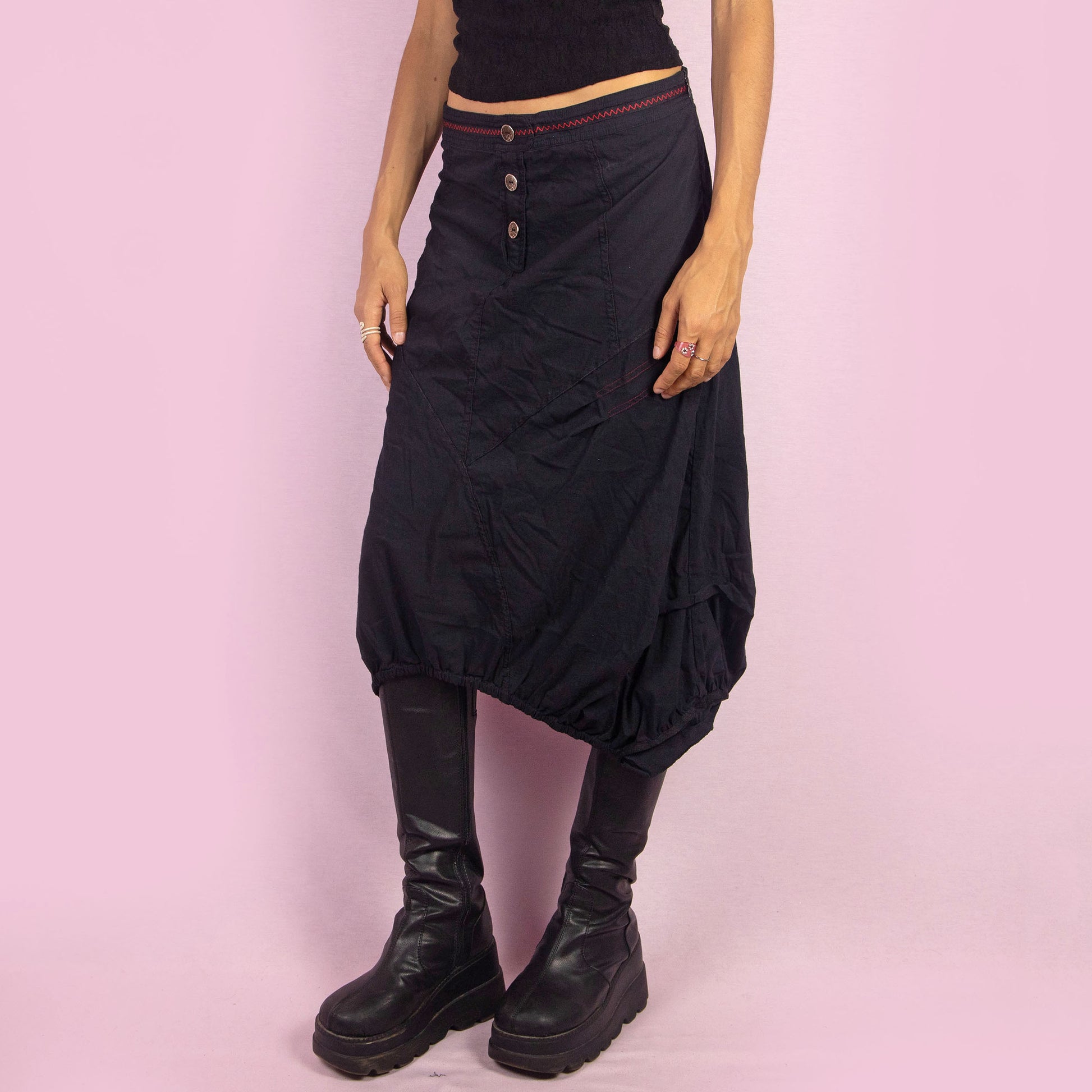 The Y2K Black Midi Balloon Skirt is a vintage 2000s piece featuring a button-front detail, stretchy fabric, and a side zipper closure. It includes pockets and has an avant-garde silhouette with a gathered hem, creating a balloon-style effect. Perfect for adding an edgy touch to casual outfits.