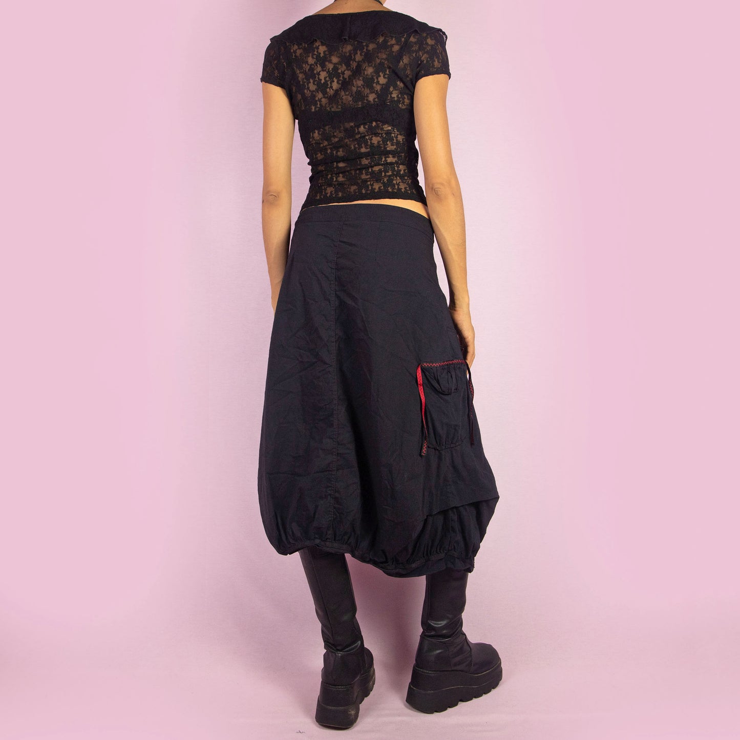 The Y2K Black Midi Balloon Skirt is a vintage 2000s piece featuring a button-front detail, stretchy fabric, and a side zipper closure. It includes pockets and has an avant-garde silhouette with a gathered hem, creating a balloon-style effect. Perfect for adding an edgy touch to casual outfits.