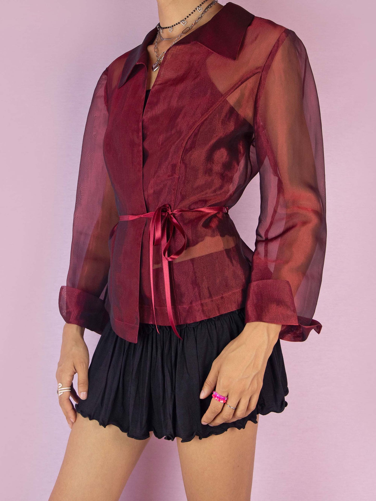 The Y2K Maroon Sheer Jacket is a vintage 2000s iridescent burgundy jacket featuring long sleeves, a pointed collar, and a tie waist. The lightweight, organza-style fabric gives it an elegant and sophisticated look, perfect for layering over evening or party outfits. Made in Spain.