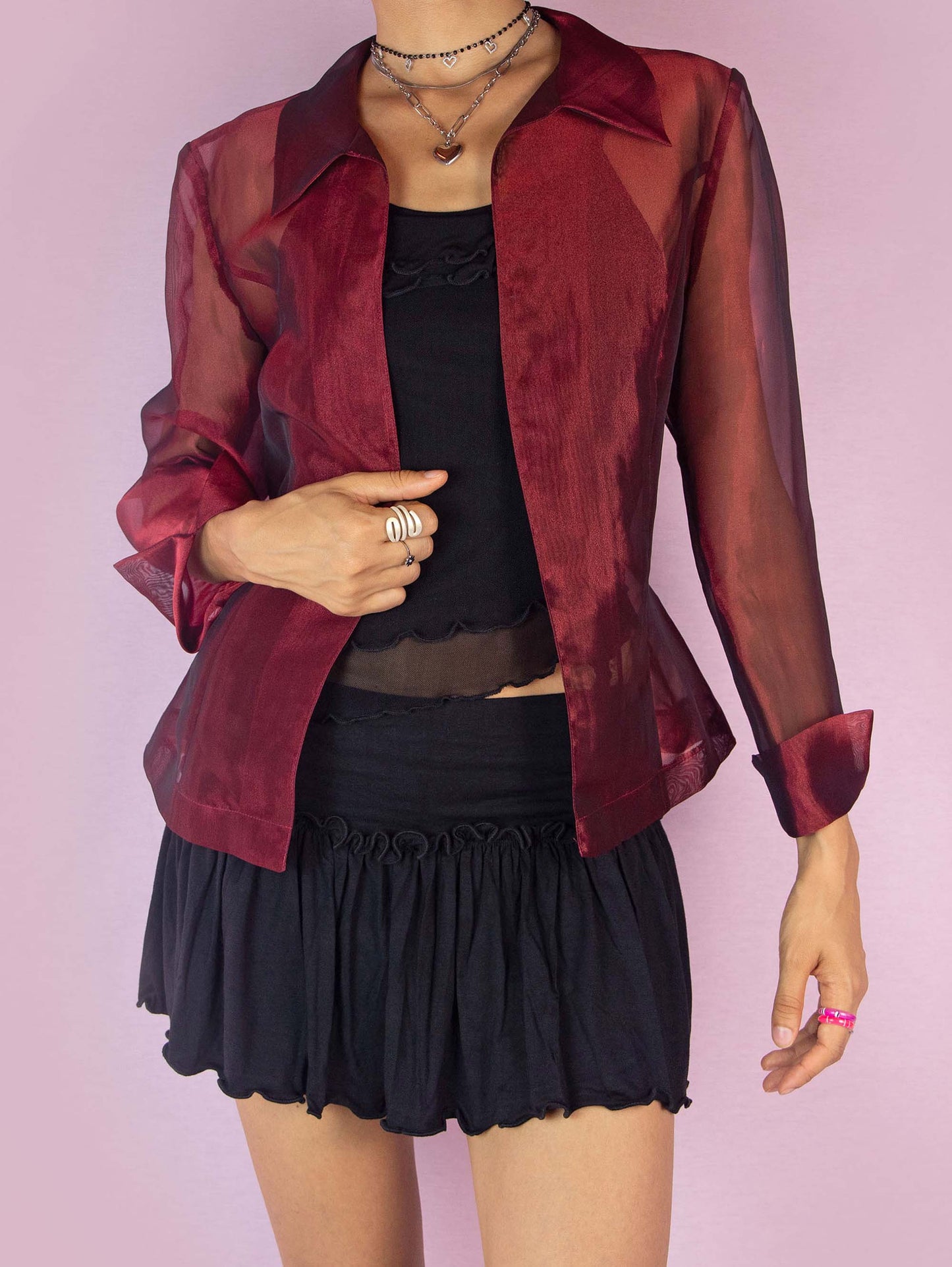 The Y2K Maroon Sheer Jacket is a vintage 2000s iridescent burgundy jacket featuring long sleeves, a pointed collar, and a tie waist. The lightweight, organza-style fabric gives it an elegant and sophisticated look, perfect for layering over evening or party outfits. Made in Spain.