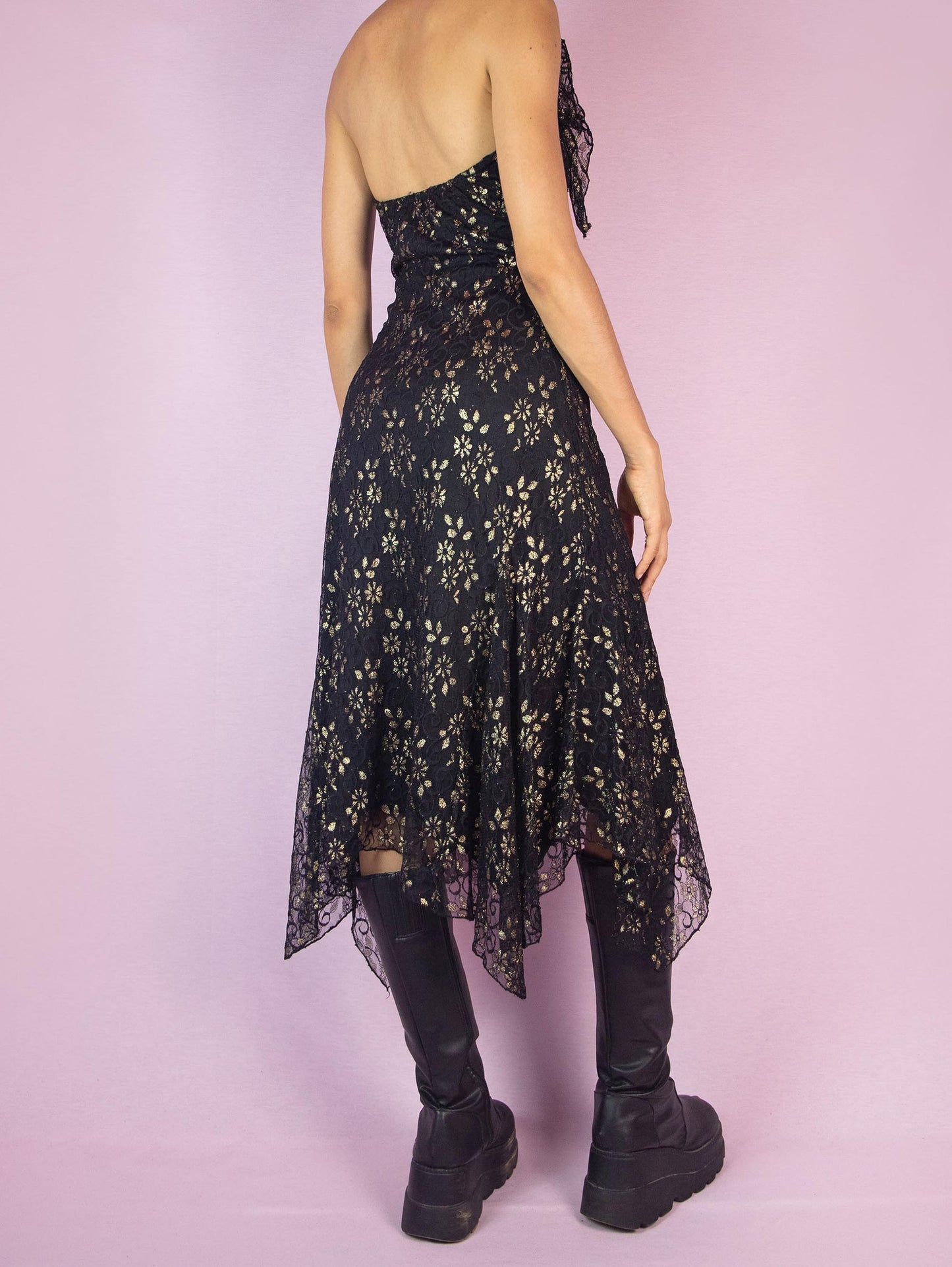 The Y2K Black Lace Asymmetrical Midi Dress is a vintage 2000s piece featuring a halter neck design and intricate golden floral lace detailing over a delicate mesh fabric. The dress is accented with ruffles along the neckline, adding a touch of romance and elegance. Perfect for a night out or special occasion.