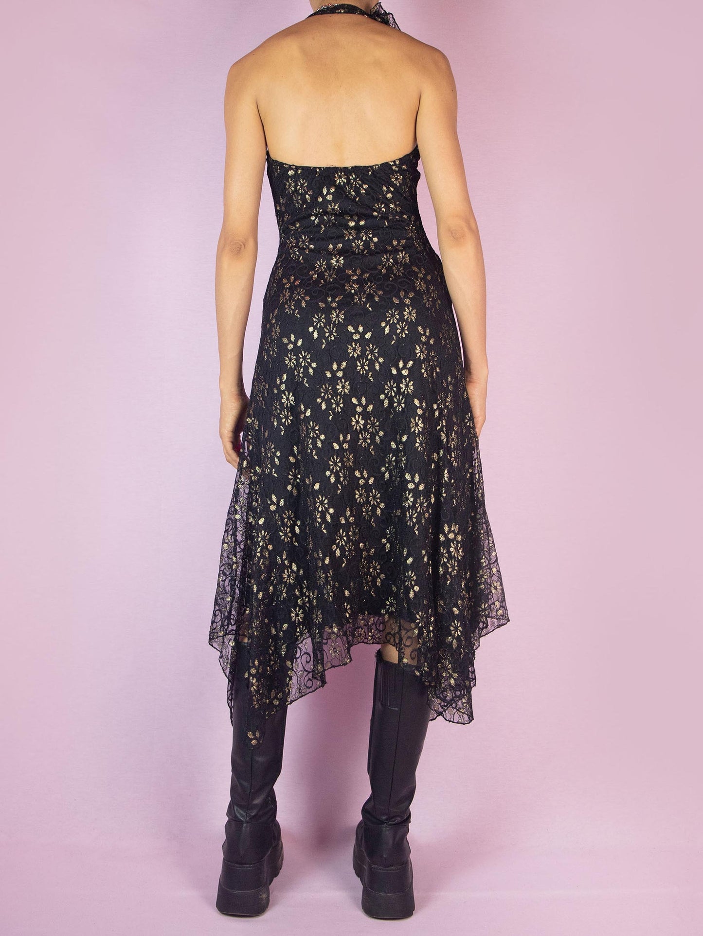 The Y2K Black Lace Asymmetrical Midi Dress is a vintage 2000s piece featuring a halter neck design and intricate golden floral lace detailing over a delicate mesh fabric. The dress is accented with ruffles along the neckline, adding a touch of romance and elegance. Perfect for a night out or special occasion.