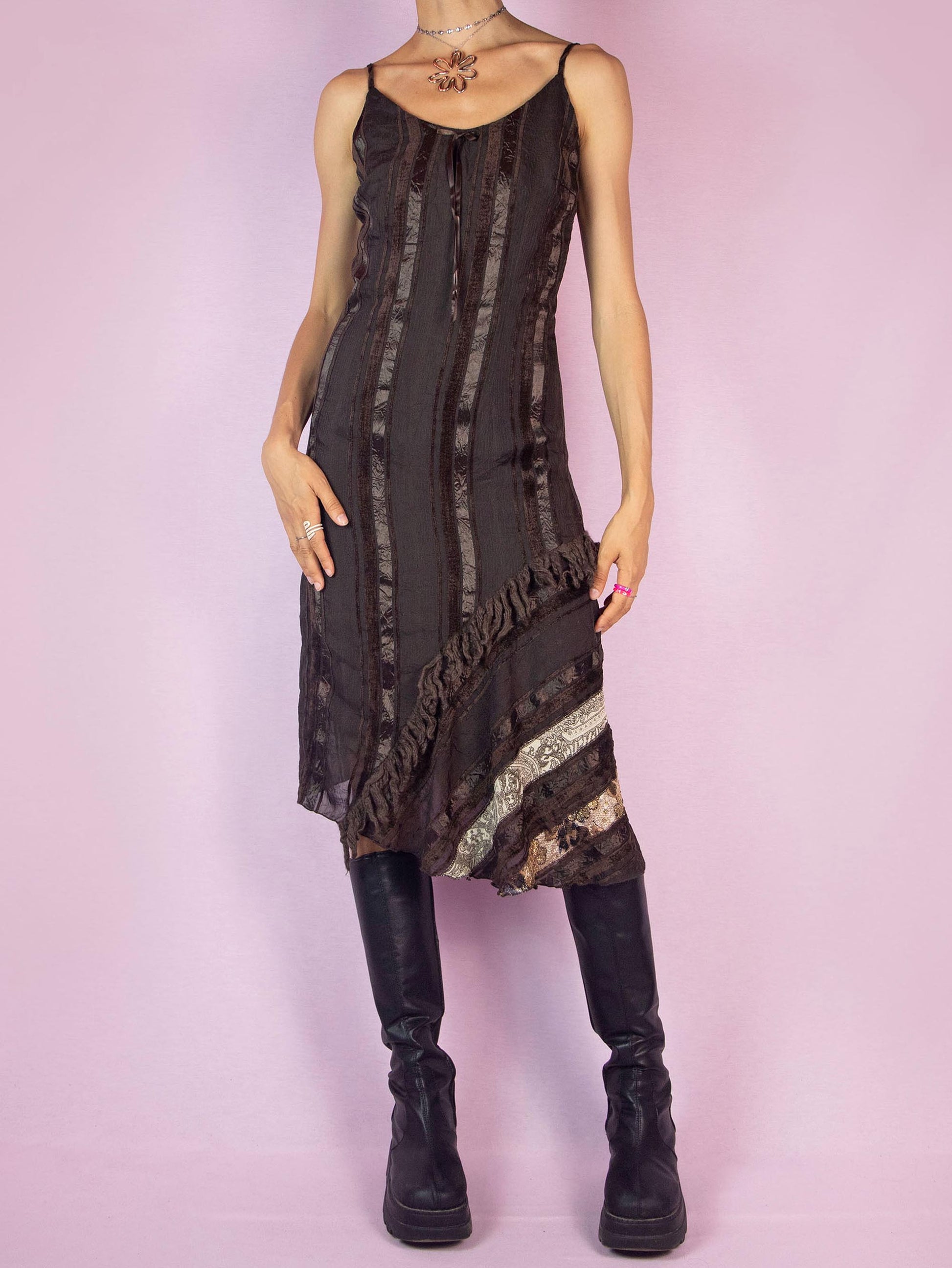 The Y2K Brown Asymmetric Midi Dress is a vintage 2000s piece featuring a striped pattern with layered textures, an asymmetrical hem, a fitted silhouette, spaghetti straps, and a back zipper closure. Perfect for adding a touch of bohemian whimsy to your party wardrobe, this dress is ideal for casual outings or evening events. Made in Spain.