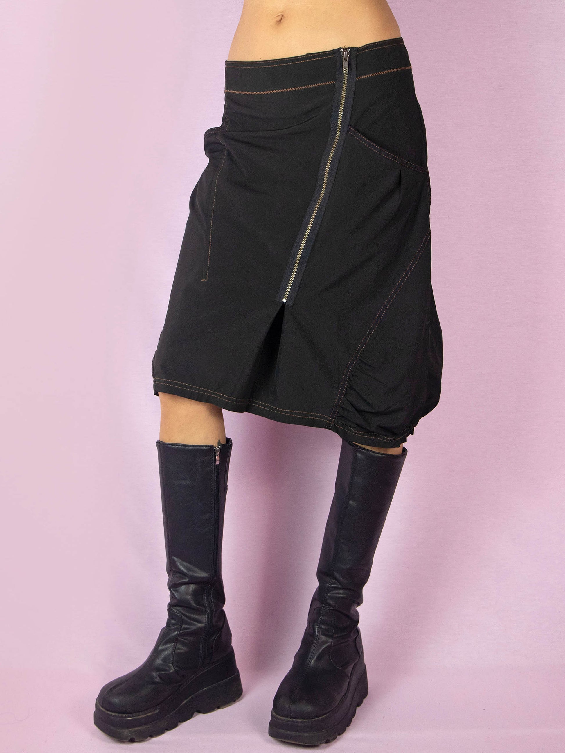 The Y2K Black Subversive Midi Skirt is a vintage 2000s avant-garde deconstructed skirt with pockets, contrast seam details, ruching at the hem, and a front zipper closure.