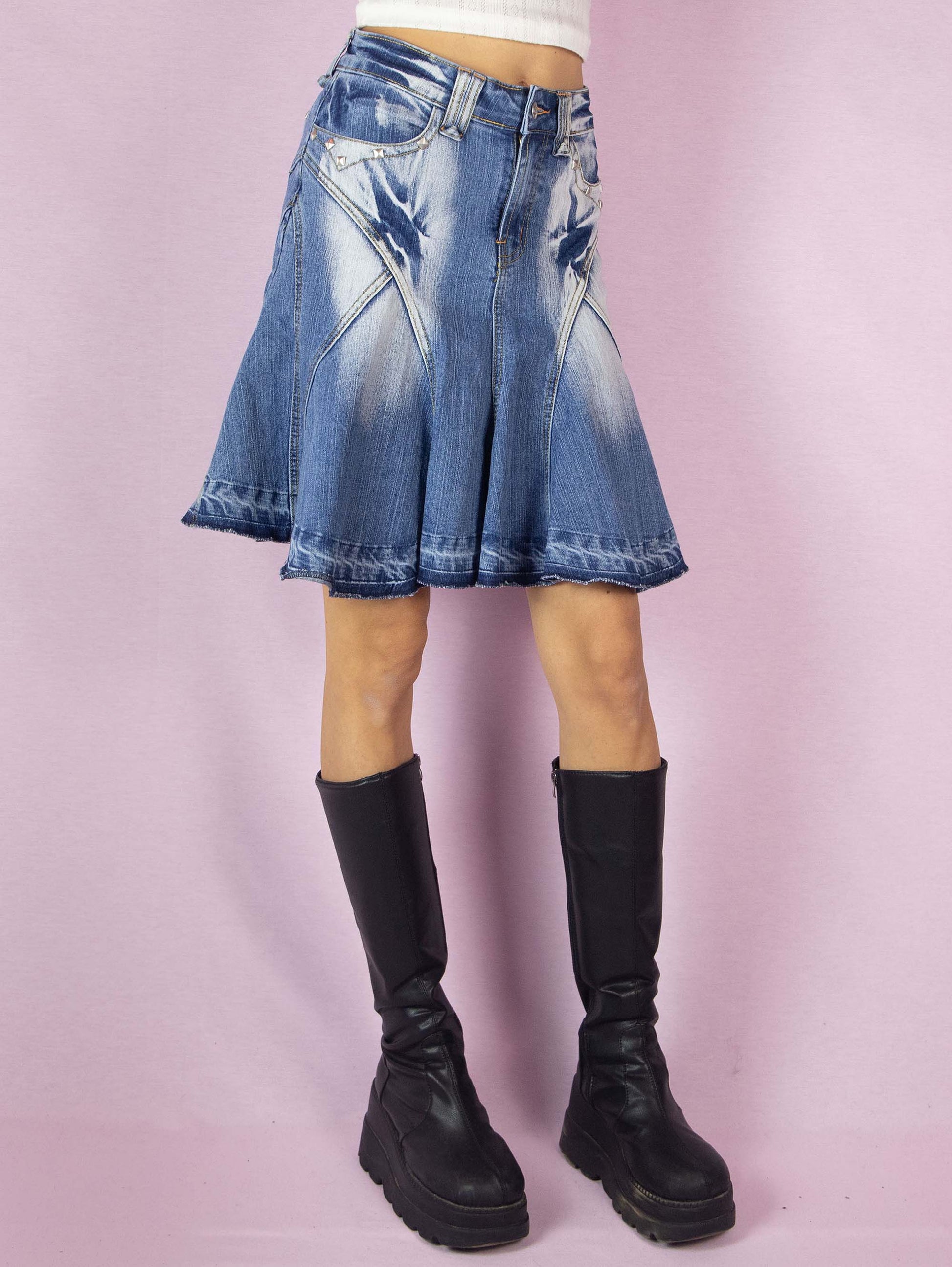The Y2K Denim Godet Trumpet Skirt is a vintage 2000s subversive deconstructed inspired jean mini skirt featuring acid wash and stud details, a raw hem, pockets, and a front zipper closure.