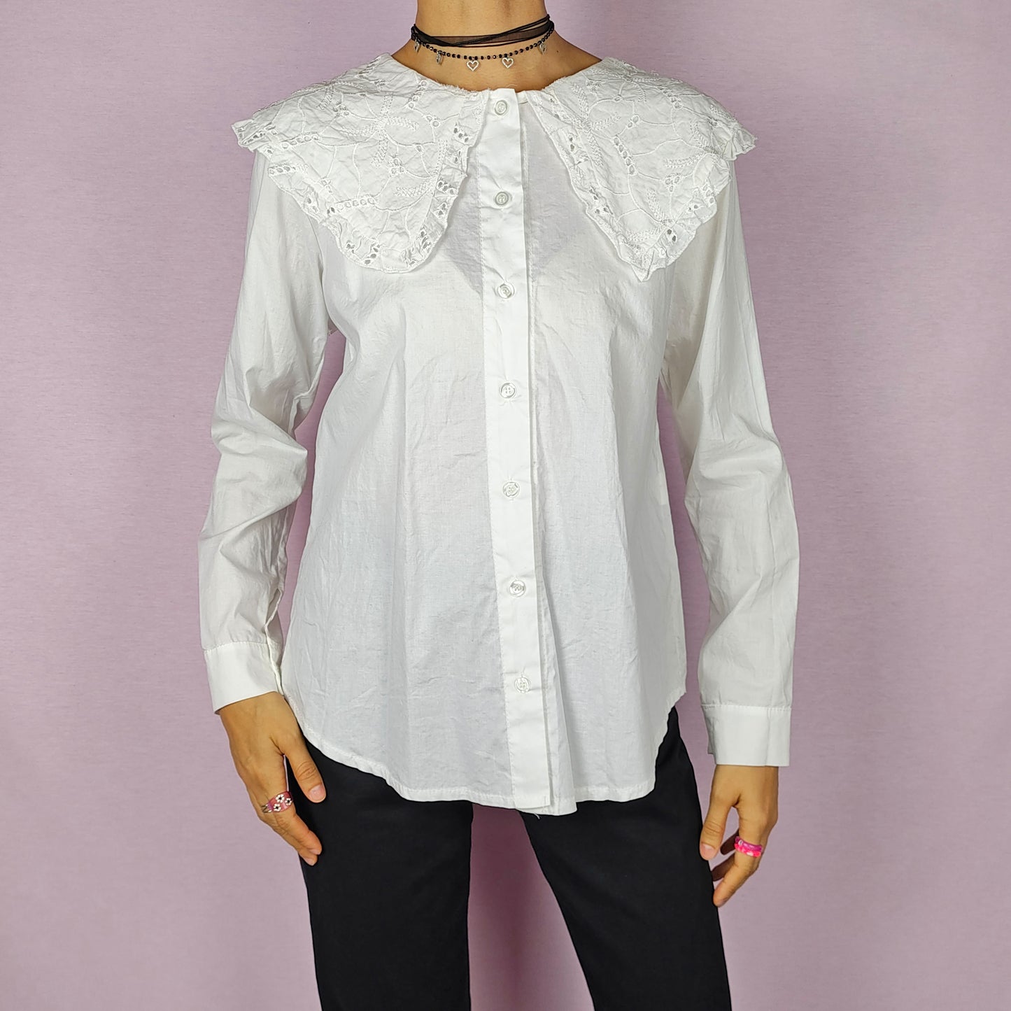 The Y2K Lace Collar White Blouse is a vintage 2000s shirt featuring an oversized lace collar in a delicate cream tone, long sleeves and a button-up front. Ideal for both casual and elegant formal wear.