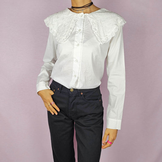 The Y2K Lace Collar White Blouse is a vintage 2000s shirt featuring an oversized lace collar in a delicate cream tone, long sleeves and a button-up front. Ideal for both casual and elegant formal wear.