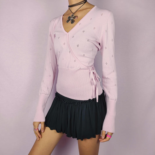 The Y2K Pink Wrap Sweater is a vintage 2000s knit pullover featuring a delicate eyelet pattern throughout. This pastel pink piece is designed with a romantic wrap-around tie detail and a ribbed waistband for a flattering, fitted silhouette. Perfect for casual or dressy looks.