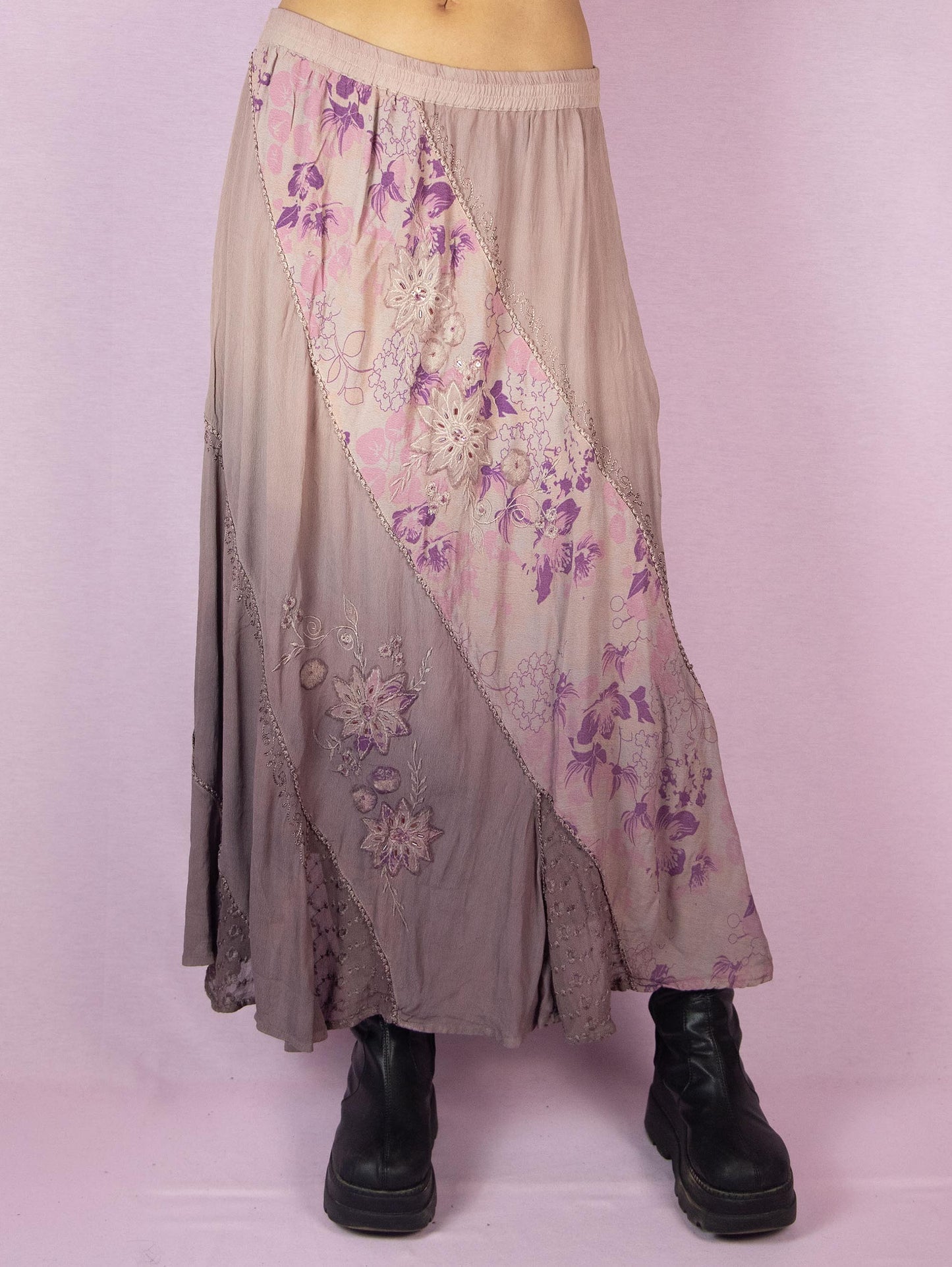 The Vintage 90s Purple A Line Midi Skirt is a dusty pinkish-purple ombre pattern boho maxi skirt with adorned with embroidered floral details, embellished with sequins and beads, and featuring an elastic waistband.