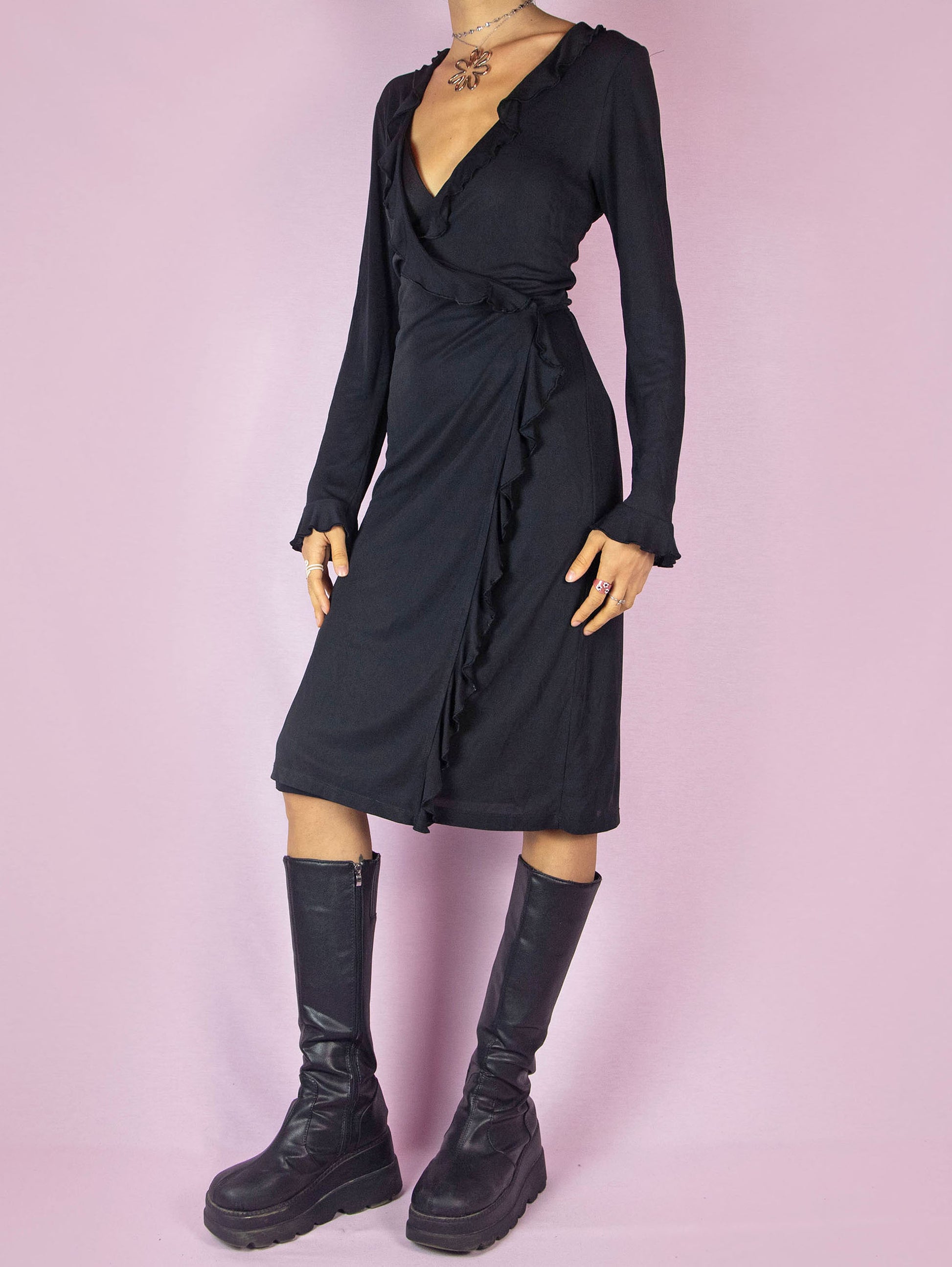 The Vintage 90s Black Ruffle Wrap Dress is a minimalist casual midi dress with long sleeves, a deep V-neckline, and is tied at the back.