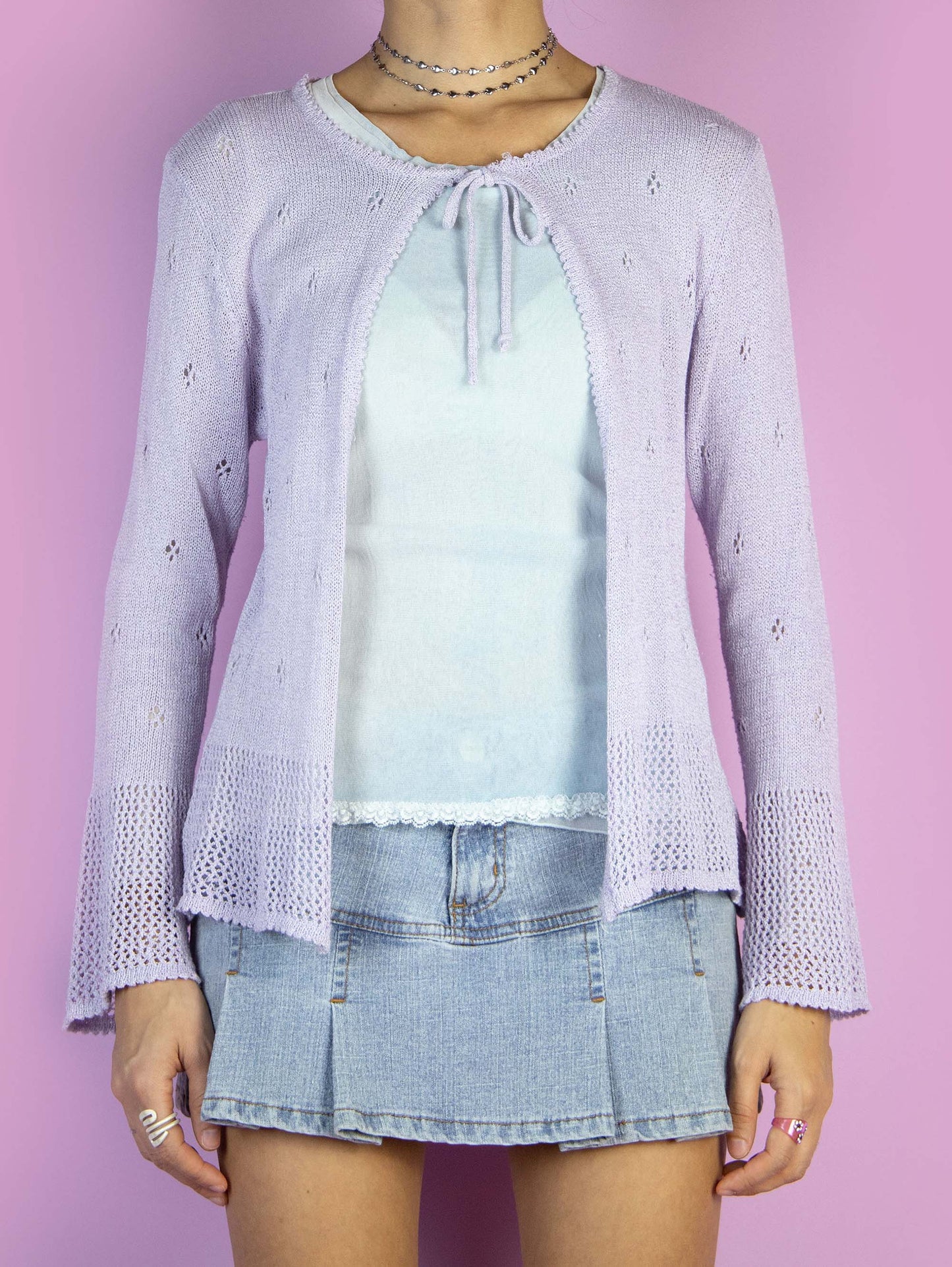 The Y2K Lilac Tie Front Cardigan is a vintage 2000s pastel light purple bolero that features a delicate knit with eyelet details, flared sleeves and has a tie closure at the neckline.