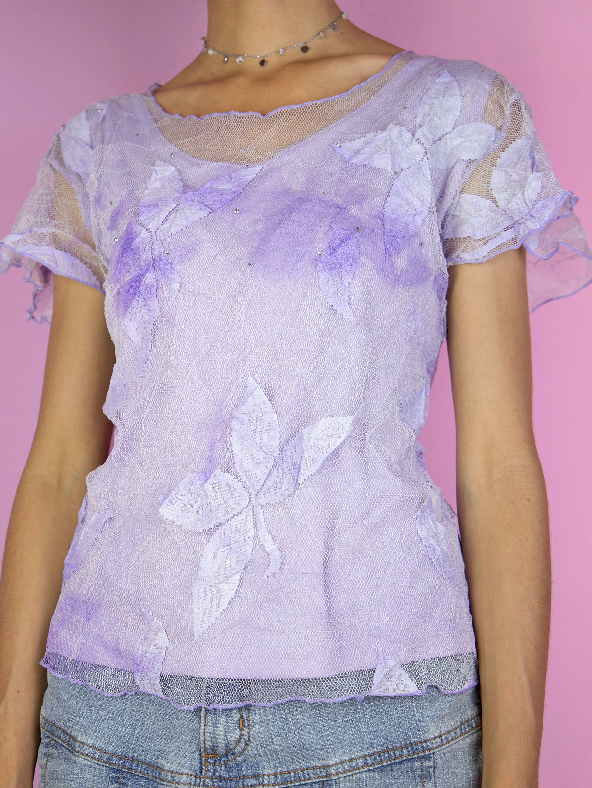 The Y2K Lilac Lace Top features short sleeves, delicate floral lace detailing, and a sheer mesh overlay. This vintage 2000s pastel light purple top is lightweight and airy, perfect for a romantic summer look.