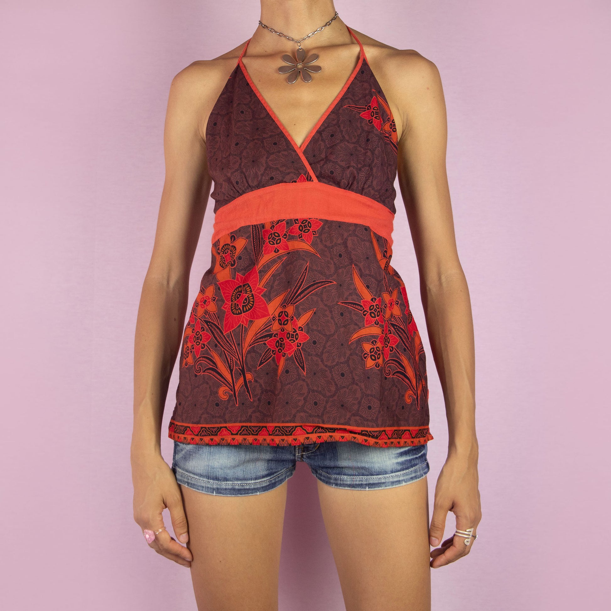 The Y2K Floral Halter Top is a vintage 2000s piece featuring a red and brown floral print, a flattering halter neckline, a tie neck for adjustable fit, and a smocked back. This lightweight and breathable top is perfect for summer days or boho-inspired looks.