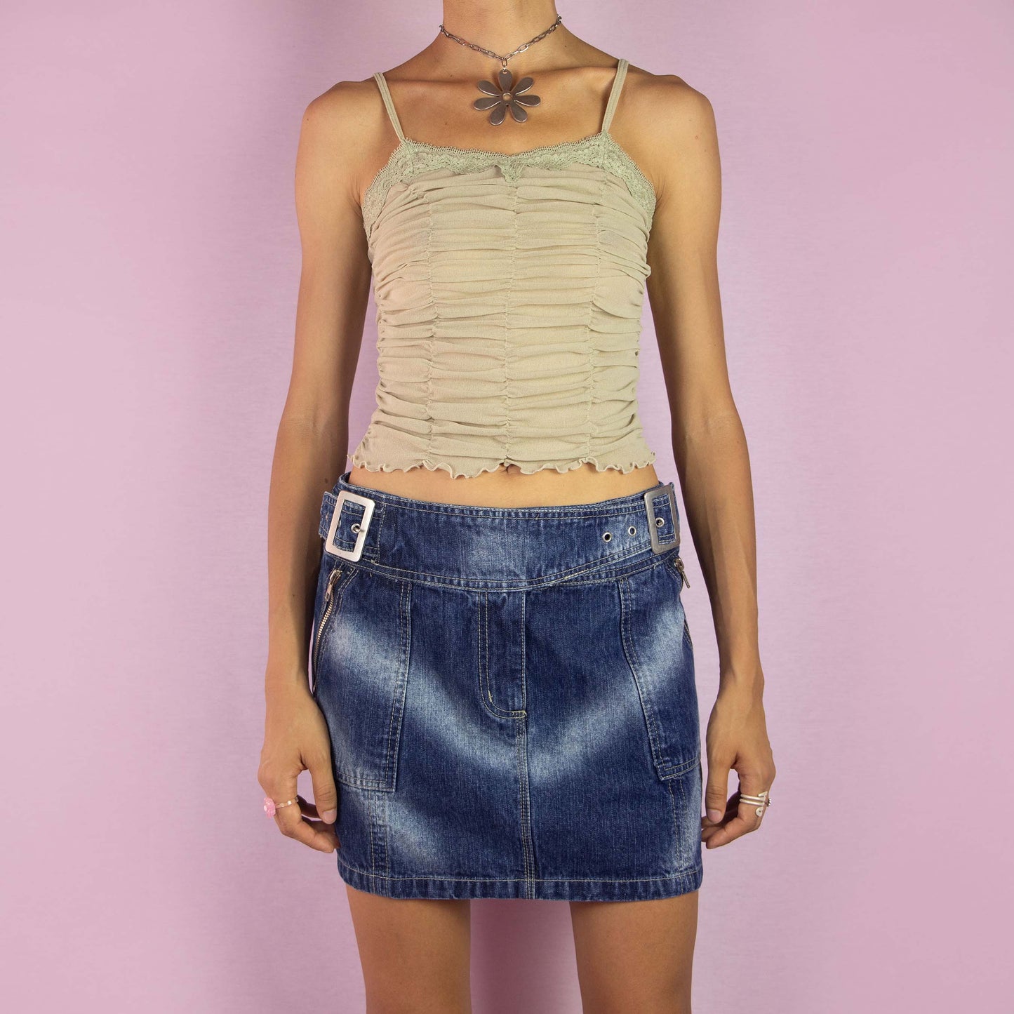 The Y2K Denim Buckle Mini Skirt is a vintage 2000s piece featuring a mid-rise fit and a structured A-line silhouette. Made from medium-wash denim, this skirt has unique buckle details at the waist, exposed zipper accents, front pockets and a back zipper closure. Perfect for casual wear and parties.