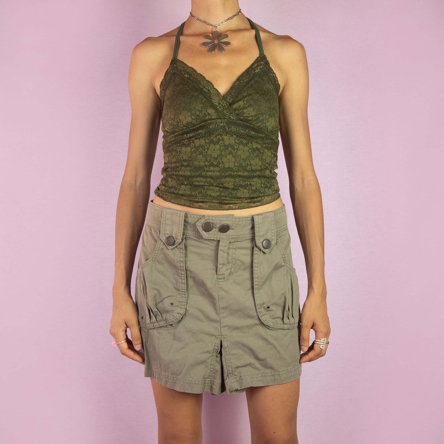 The Y2K Cargo Khaki Mini Skirt is a vintage 2000s piece featuring a mid-rise fit and a mini length silhouette. Made from green cotton, the skirt is designed with cargo-style front pockets and decorative button details. It includes a front button and zipper closure, making it perfect for casual wear and outdoor adventures.