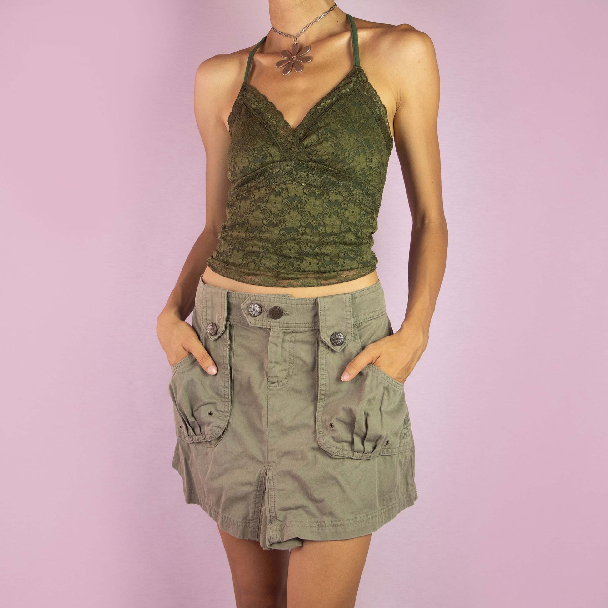 The Y2K Cargo Khaki Mini Skirt is a vintage 2000s piece featuring a mid-rise fit and a mini length silhouette. Made from green cotton, the skirt is designed with cargo-style front pockets and decorative button details. It includes a front button and zipper closure, making it perfect for casual wear and outdoor adventures.