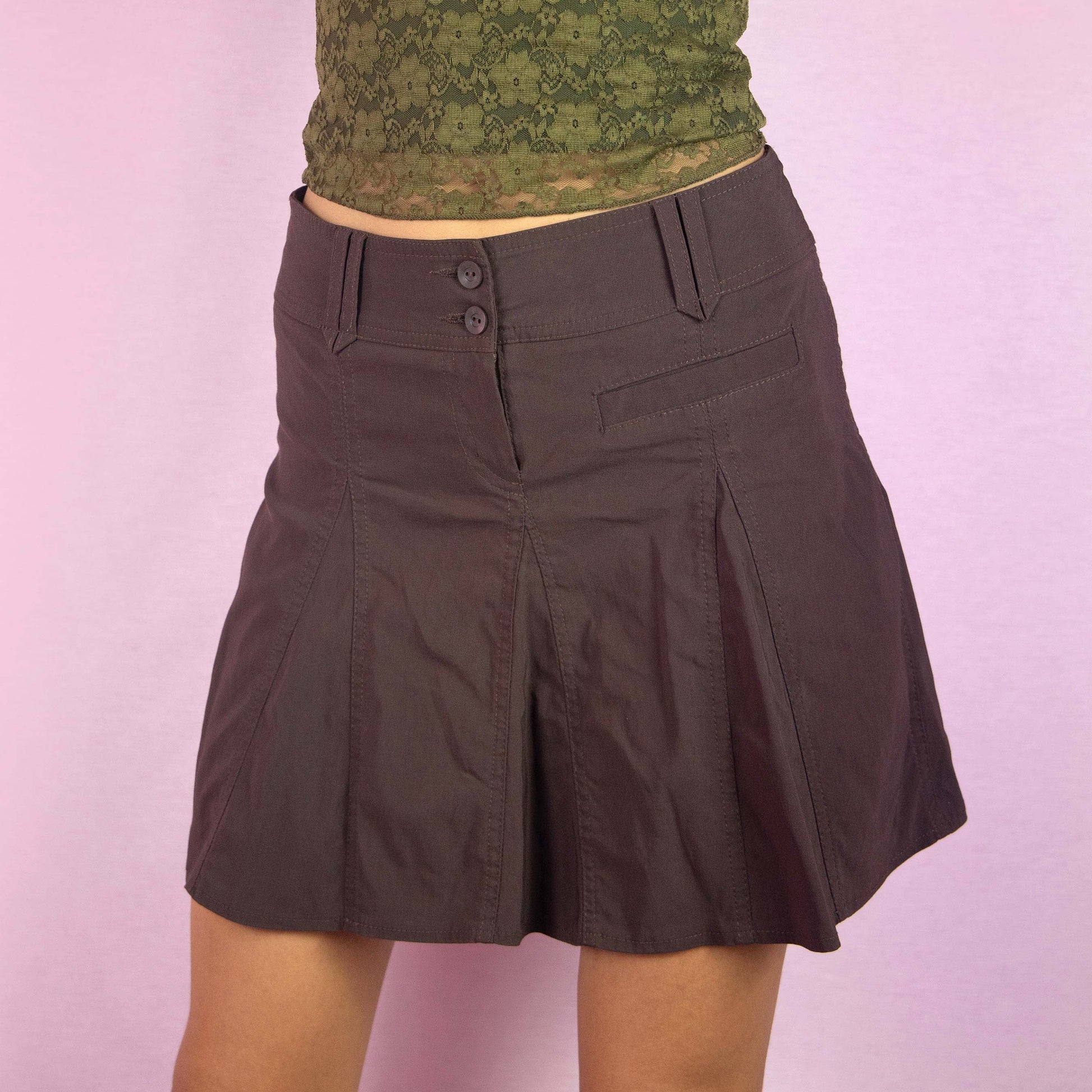 The Y2K Flare Brown Mini Skirt is a vintage 2000s piece featuring a high-rise fit, stretchy fabric, and a flared A-line godet silhouette. The skirt includes pleated detailing along the front and back, with a double-button and zipper closure. Ideal for casual wear and summer outings.