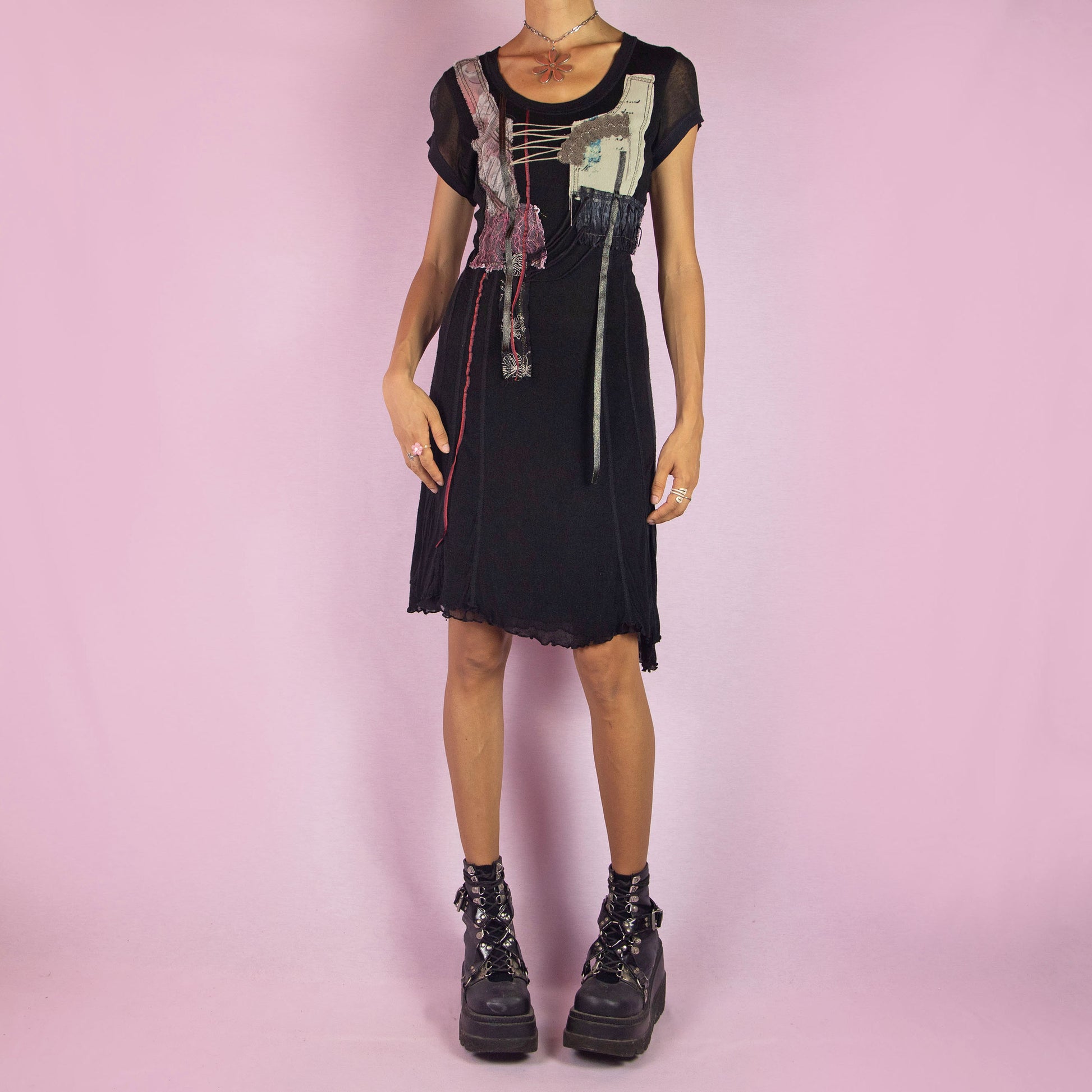 The Y2K Black Knit Dress is a vintage 2000s layered mini dress featuring a stretchy silk-knit fabric and short sleeves. Adorned with patchwork details, lace-up accents, and raw edges, it has an eclectic, whimsical look. The unique blend of textures and asymmetrical lines make it perfect for casual outings and evening event. Made in Spain.