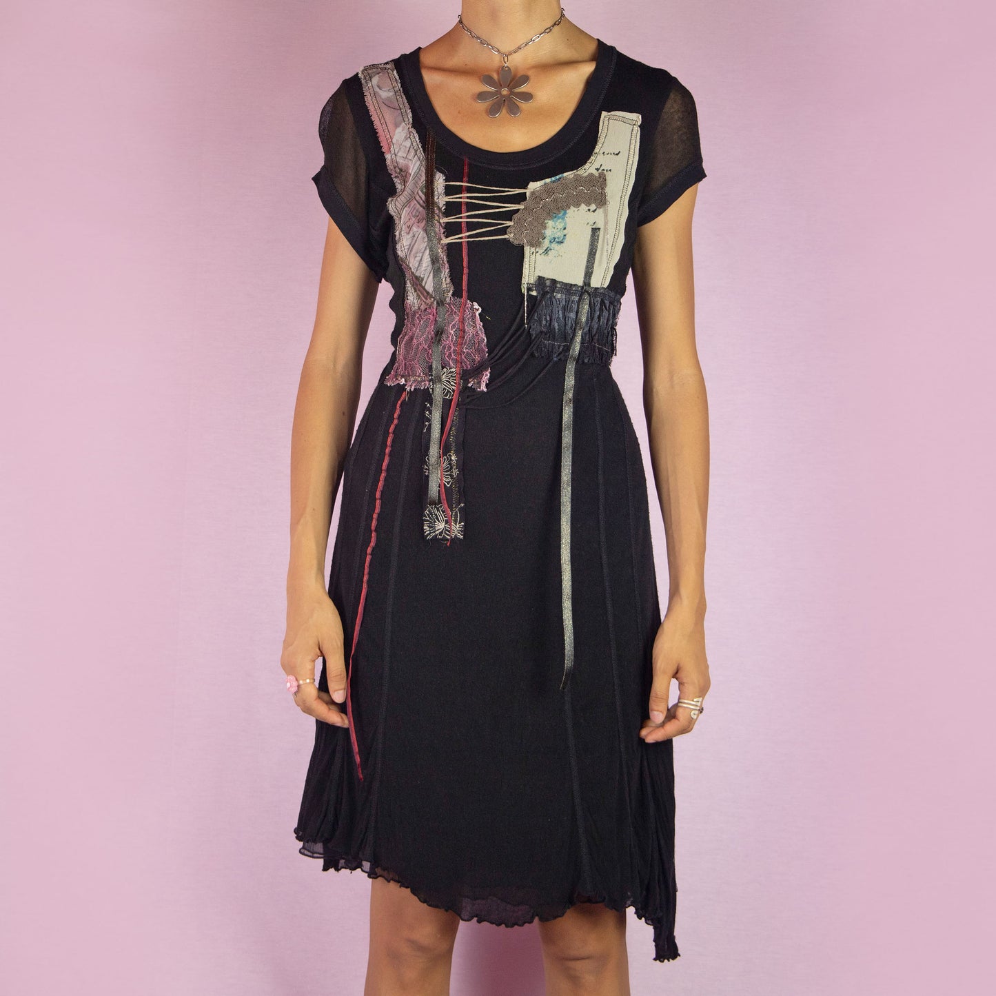 The Y2K Black Knit Dress is a vintage 2000s layered mini dress featuring a stretchy silk-knit fabric and short sleeves. Adorned with patchwork details, lace-up accents, and raw edges, it has an eclectic, whimsical look. The unique blend of textures and asymmetrical lines make it perfect for casual outings and evening event. Made in Spain.