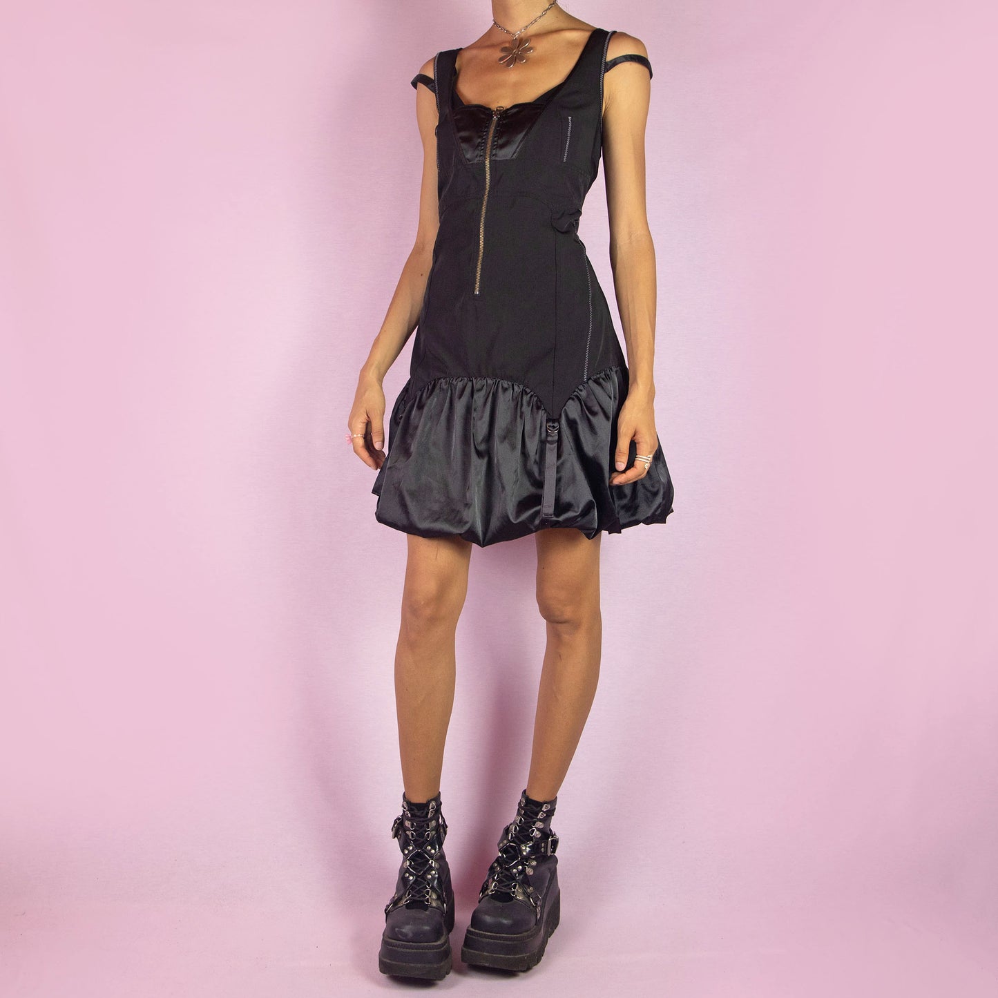 The Y2K Black Bubble Mini Dress is a vintage 2000s piece featuring a fitted bodice with a satin finish and front zipper. It has double straps and a distinctive bubble hemline with ruching and buckle details. Its structured design and sleek silhouette make it ideal for evening events and nights out.