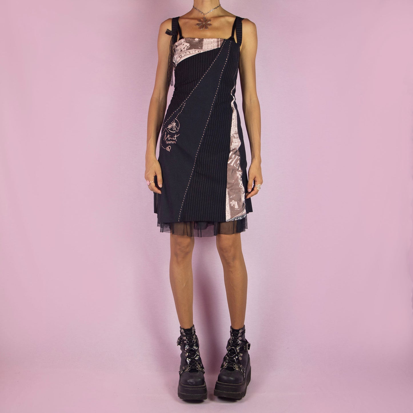 The Y2K Black Layered Mini Dress is a vintage 2000s piece featuring a square neckline, straps, and stretchy fabric. It showcases a layered design with pinstripe and abstract printed panels, complemented by a tulle mesh underlayer for added volume. Ideal for parties and night events.