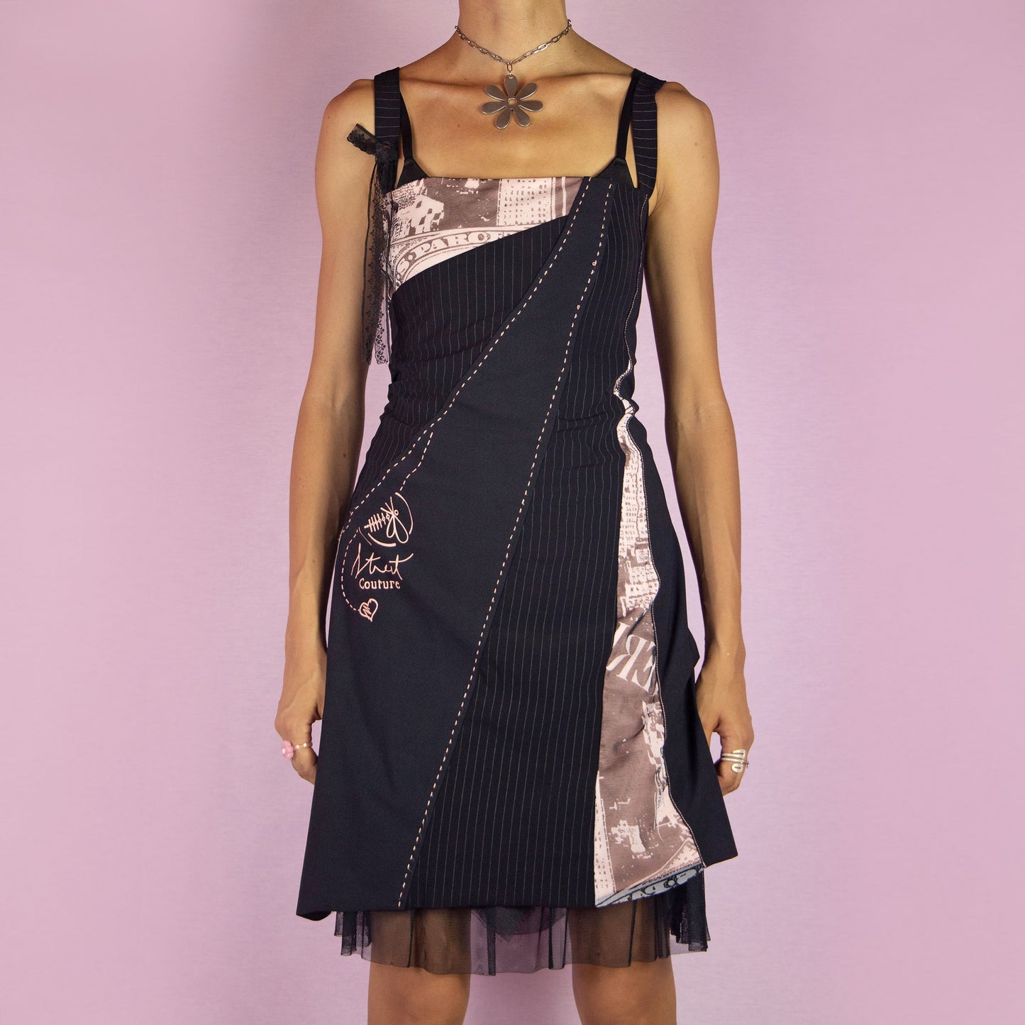 The Y2K Black Layered Mini Dress is a vintage 2000s piece featuring a square neckline, straps, and stretchy fabric. It showcases a layered design with pinstripe and abstract printed panels, complemented by a tulle mesh underlayer for added volume. Ideal for parties and night events.