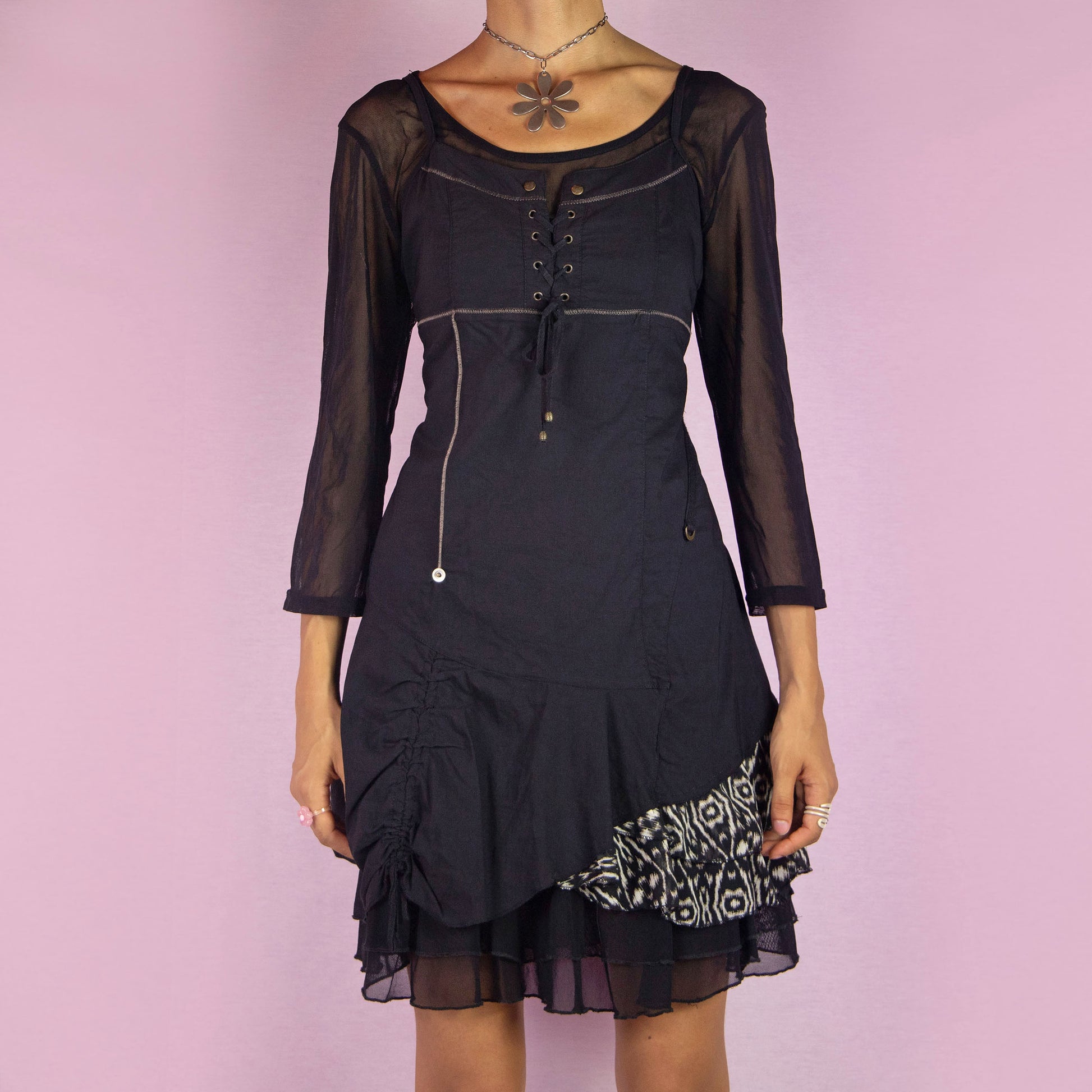 The Y2K Black Asymmetric Mesh Dress is a vintage 2000s mini dress featuring a scoop neckline, three-quarter sheer mesh sleeves, and a stretchy fabric. It has a lace-up bodice, side zipper closure, and an asymmetric hemline with gathered details and a printed panel. The layered mesh underlay gives it a whimsical touch, making it perfect for parties and night events.