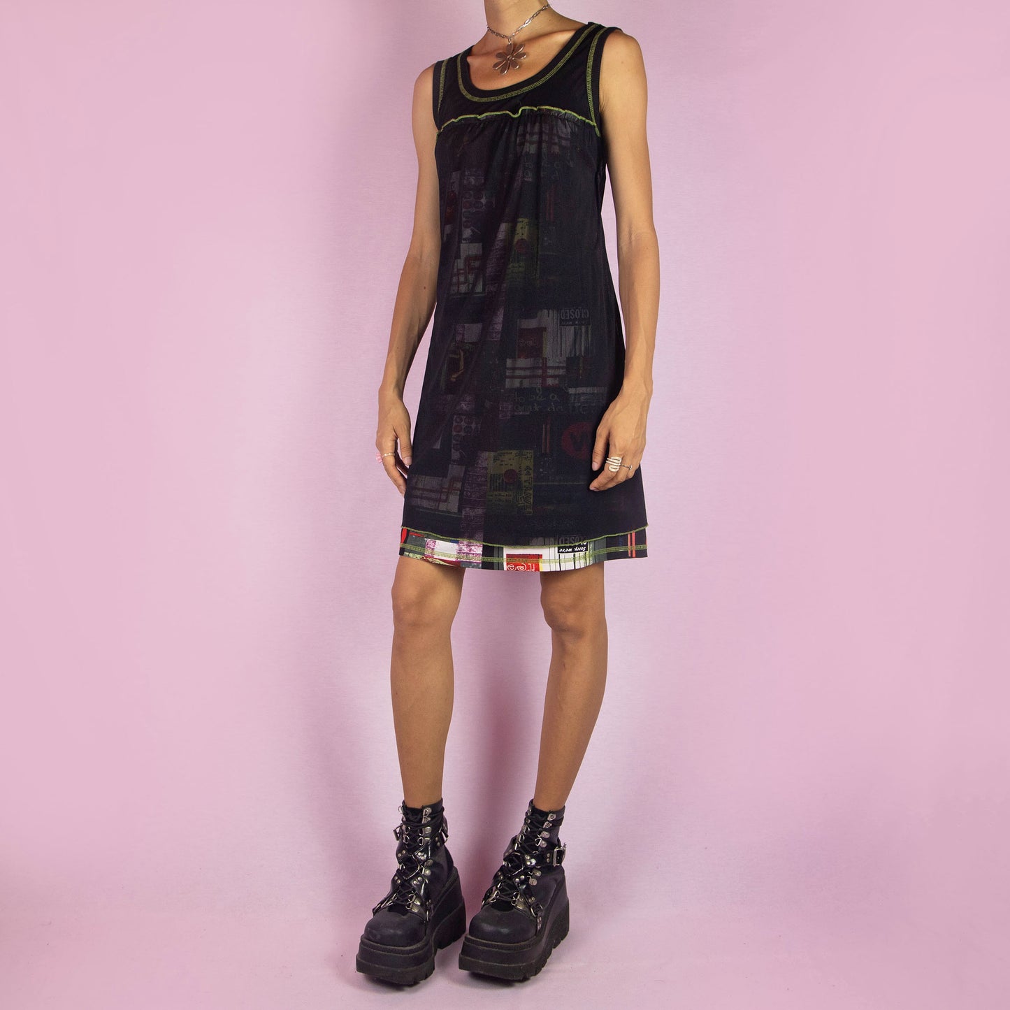 The Y2K Black Sleeveless Mesh Dress is a vintage 2000s mini dress featuring a scoop neckline, relaxed fit, and lightweight mesh fabric. The dress is adorned with abstract prints and neon green stitching along the neckline and hem. Its layered design and playful details make it perfect for casual summer outings.