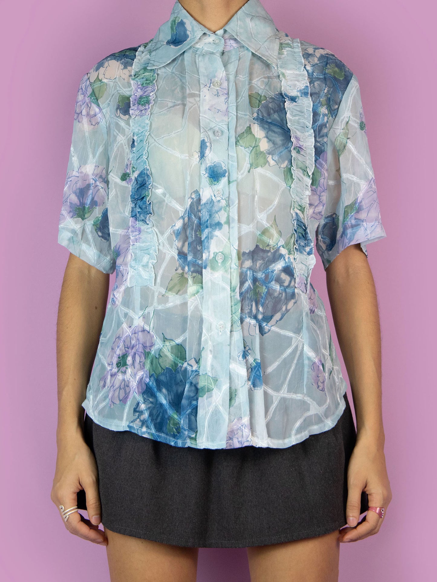 The Y2K Print Sheer Blouse is a vintage 2000s boho summer style light blue floral graphic semi-transparent short-sleeve top with a collar, buttons, and gathered ruffle details.