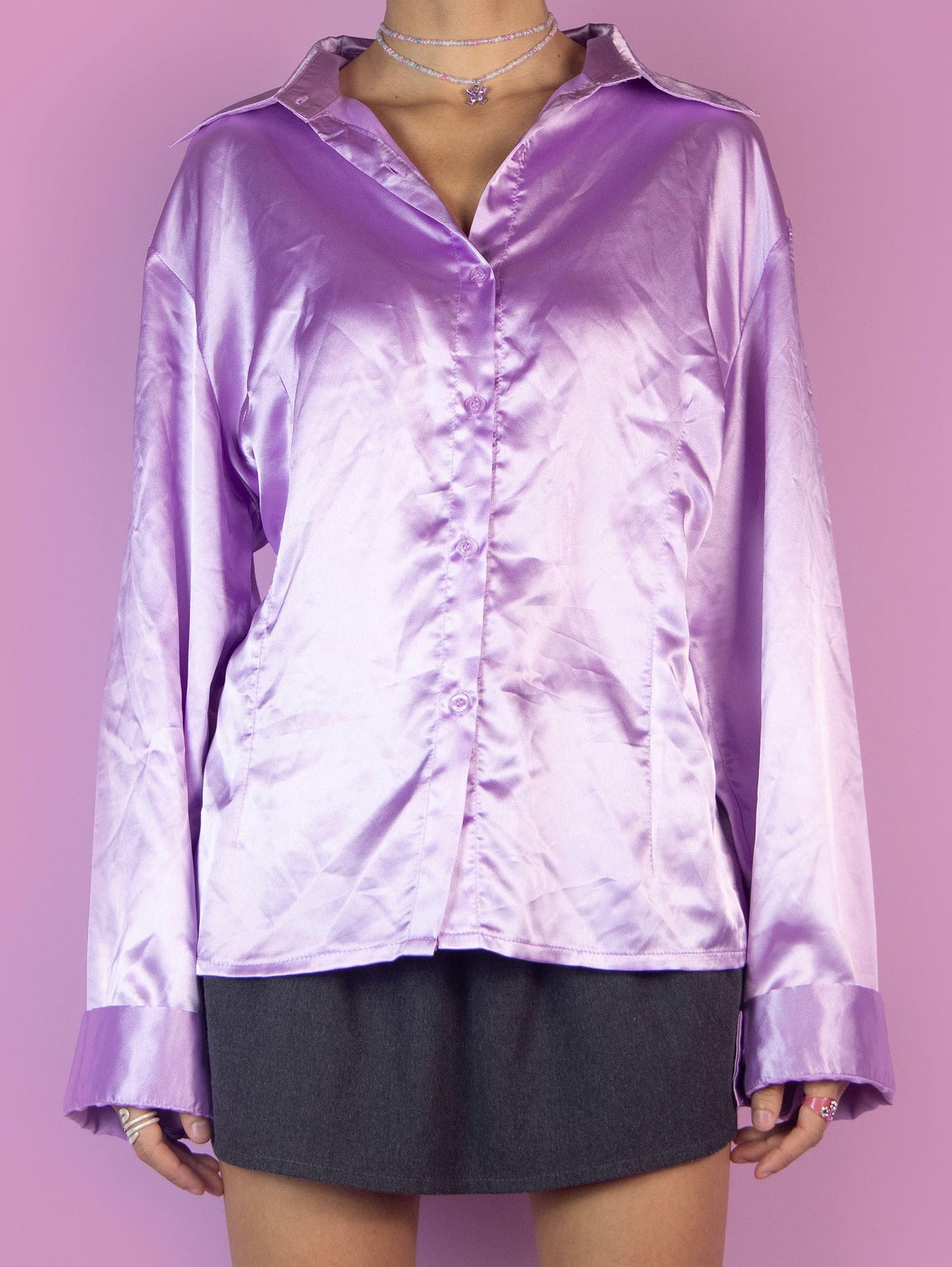 The Y2K Lilac Satin Blouse features a button-down front, long sleeves, and a pointed collar. This vintage 2000s purple shirt has a shiny, smooth texture, adding a touch of elegance to any office work outfit.