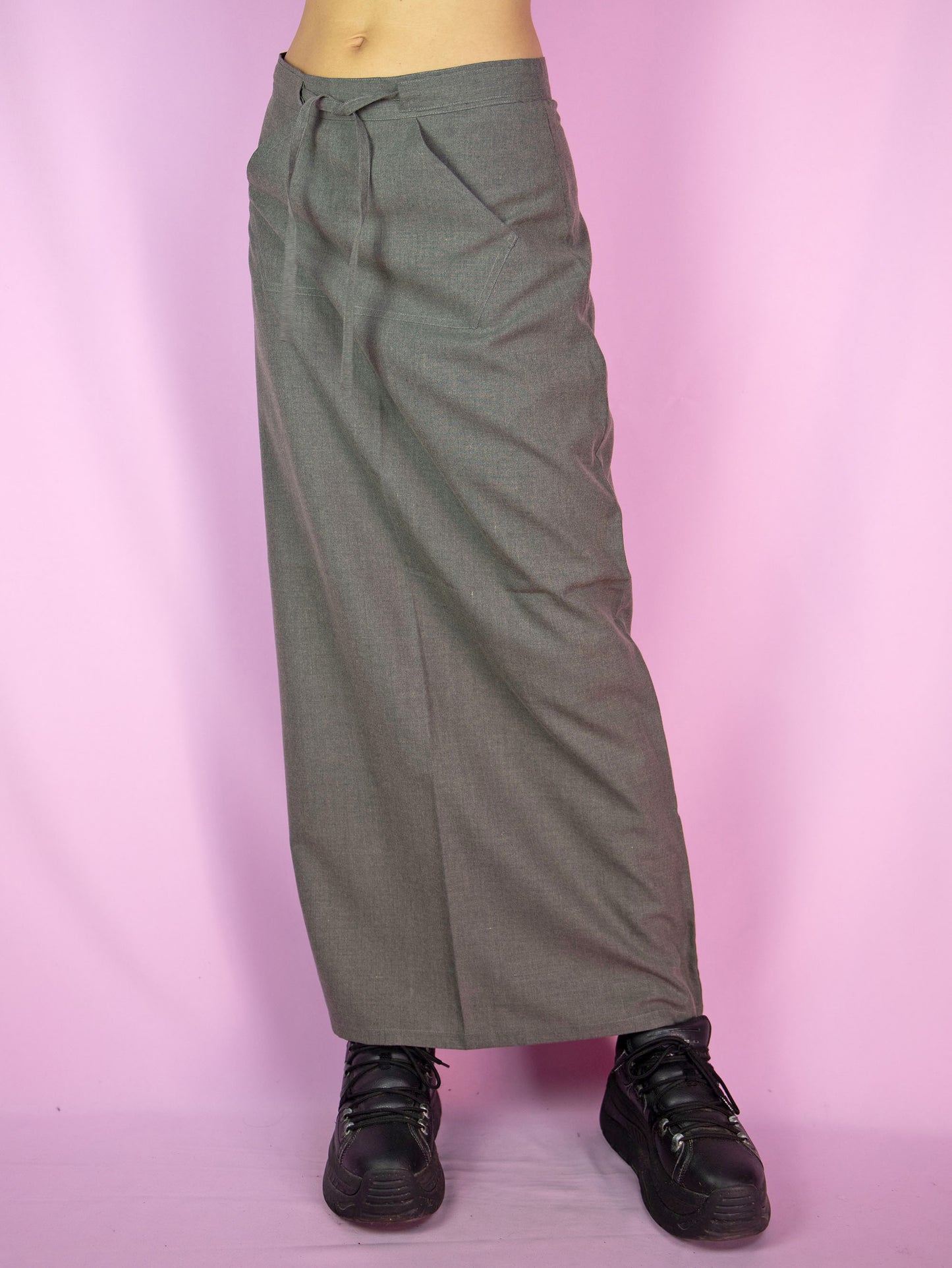 The Vintage 90s Gray Maxi Skirt is a slit-back skirt in gray that ties in the front, featuring a pocket and back zipper closure. Cyber grunge 1990s cargo midi skirt.