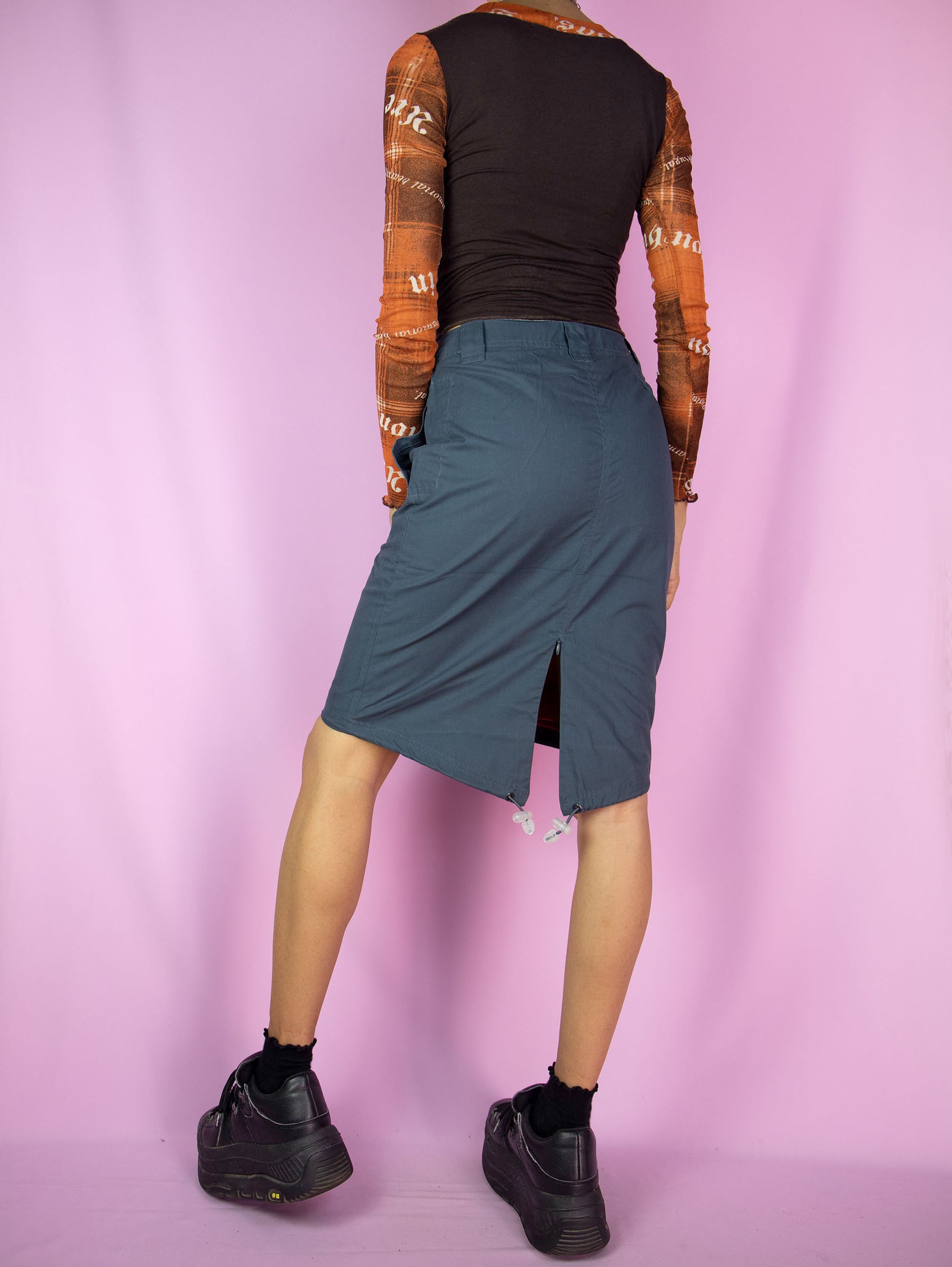 The Y2K Blue Grunge Utility Skirt is a vintage asymmetric dark blue-gray skirt with pockets, a back slit and front zipper closure. Cyber gorpcore 2000s cargo mini skirt.