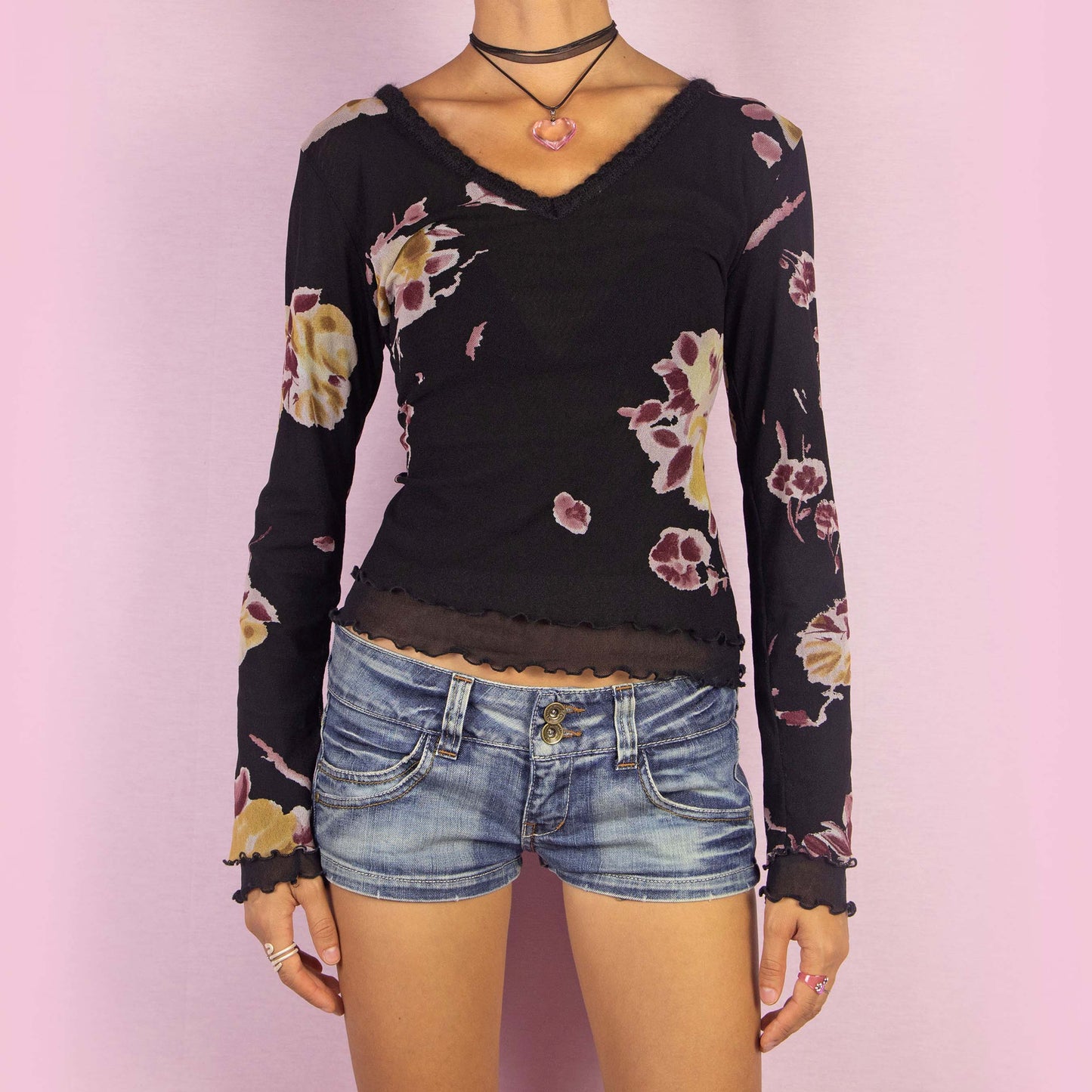 The Y2K Black Mesh Floral Top is a vintage 2000s long-sleeve shirt featuring a semi-sheer double-layered mesh fabric with a floral print in muted tones. Designed with a flattering V-neckline, lettuce hem details, and a slim fit, this piece is perfect for casual outings or evening events.