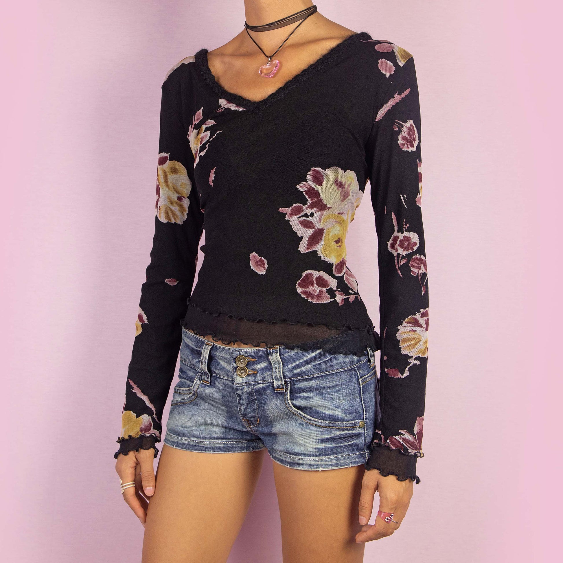 The Y2K Black Mesh Floral Top is a vintage 2000s long-sleeve shirt featuring a semi-sheer double-layered mesh fabric with a floral print in muted tones. Designed with a flattering V-neckline, lettuce hem details, and a slim fit, this piece is perfect for casual outings or evening events.