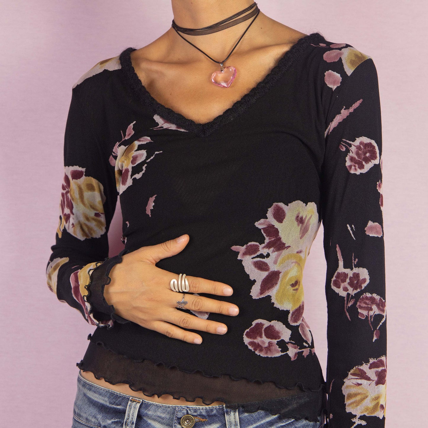 The Y2K Black Mesh Floral Top is a vintage 2000s long-sleeve shirt featuring a semi-sheer double-layered mesh fabric with a floral print in muted tones. Designed with a flattering V-neckline, lettuce hem details, and a slim fit, this piece is perfect for casual outings or evening events.