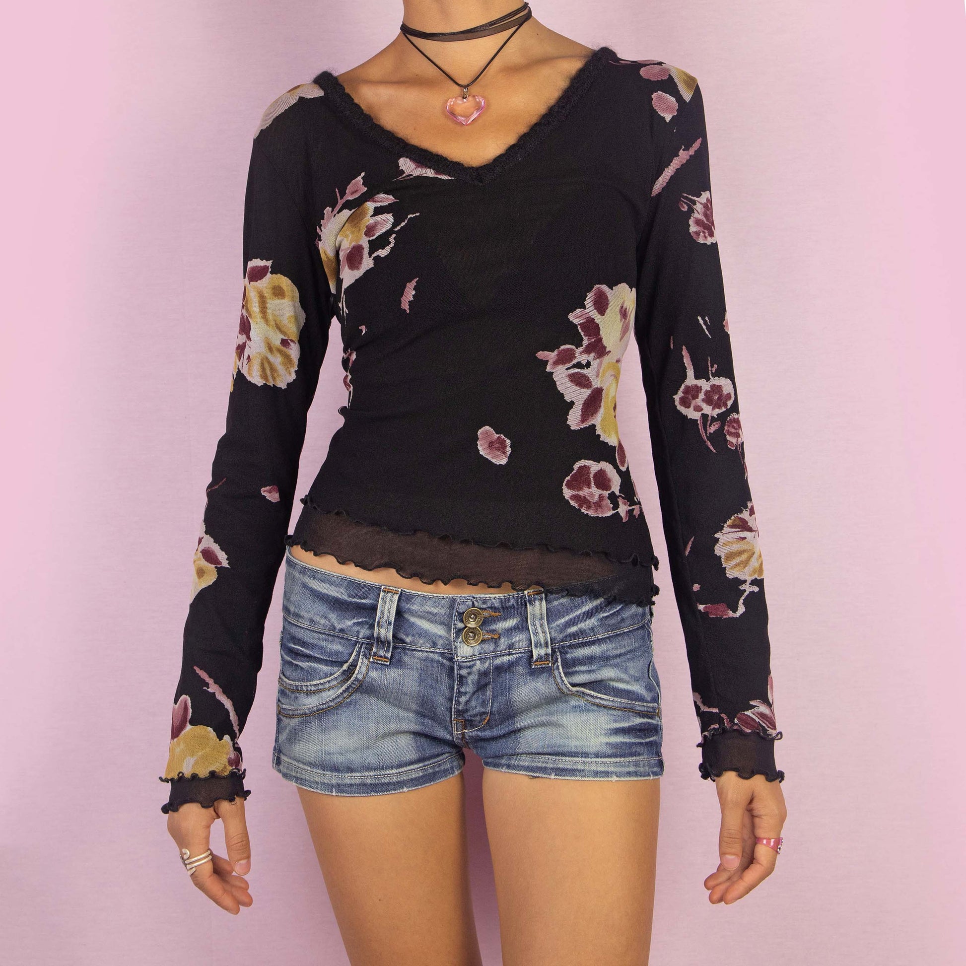 The Y2K Black Mesh Floral Top is a vintage 2000s long-sleeve shirt featuring a semi-sheer double-layered mesh fabric with a floral print in muted tones. Designed with a flattering V-neckline, lettuce hem details, and a slim fit, this piece is perfect for casual outings or evening events.