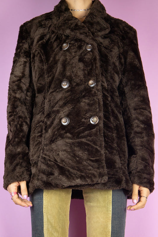 The Vintage 90s Brown Faux Fur Jacket is a dark brown faux fur coat featuring a classic collar, double row button closure, and pockets. Ideal for a casual winter wardrobe.