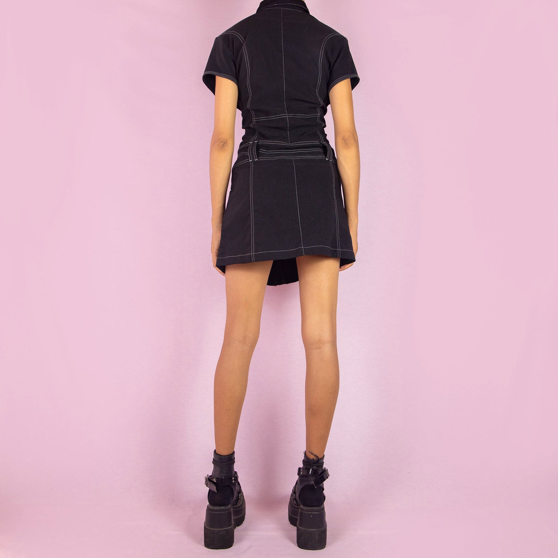 The Vintage 90s Black Utility Mini Dress is a sleek, structured piece featuring a collared neckline, short sleeves, and snap button closure along the front. The dress is designed with contrast stitching and stretchy fabric. Chest pockets and belt loops add a utilitarian touch, while the fitted silhouette and mini length make it perfect for casual outings or night events.