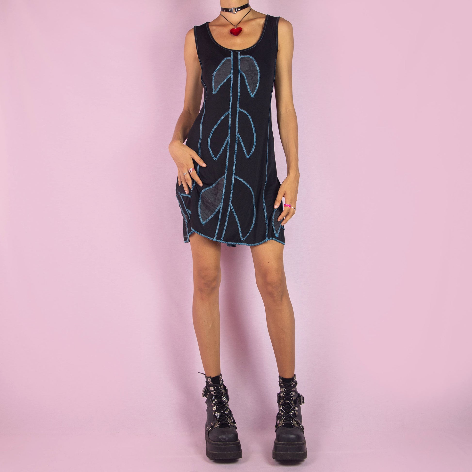 The Y2K Black Mini Sleeveless Dress is a vintage 2000s piece featuring a scoop neckline. This mini dress showcases a bold blue contrast-stitched design and is made from stretchy fabric. It includes a tie-back detail for an adjustable fit. Perfect for summer casual outings.