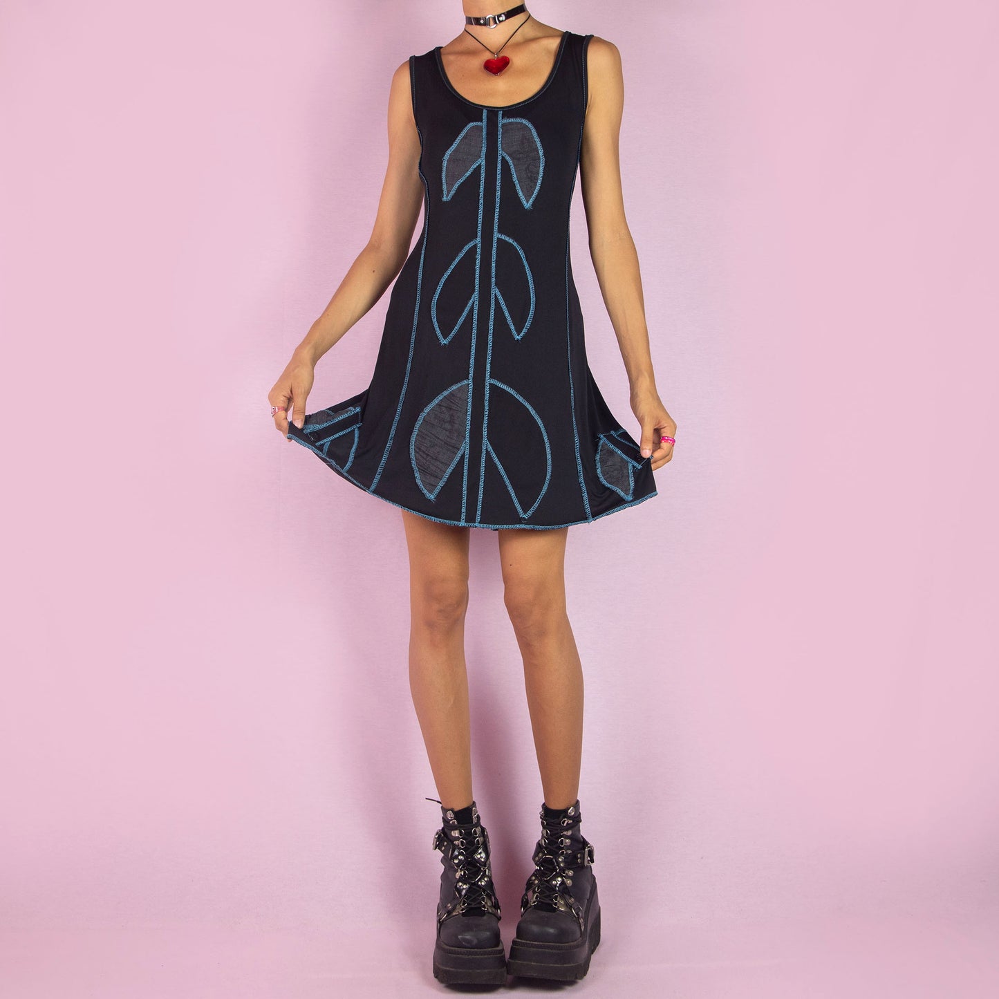 The Y2K Black Mini Sleeveless Dress is a vintage 2000s piece featuring a scoop neckline. This mini dress showcases a bold blue contrast-stitched design and is made from stretchy fabric. It includes a tie-back detail for an adjustable fit. Perfect for summer casual outings.