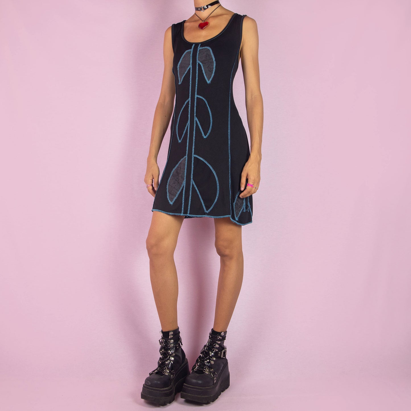 The Y2K Black Mini Sleeveless Dress is a vintage 2000s piece featuring a scoop neckline. This mini dress showcases a bold blue contrast-stitched design and is made from stretchy fabric. It includes a tie-back detail for an adjustable fit. Perfect for summer casual outings.