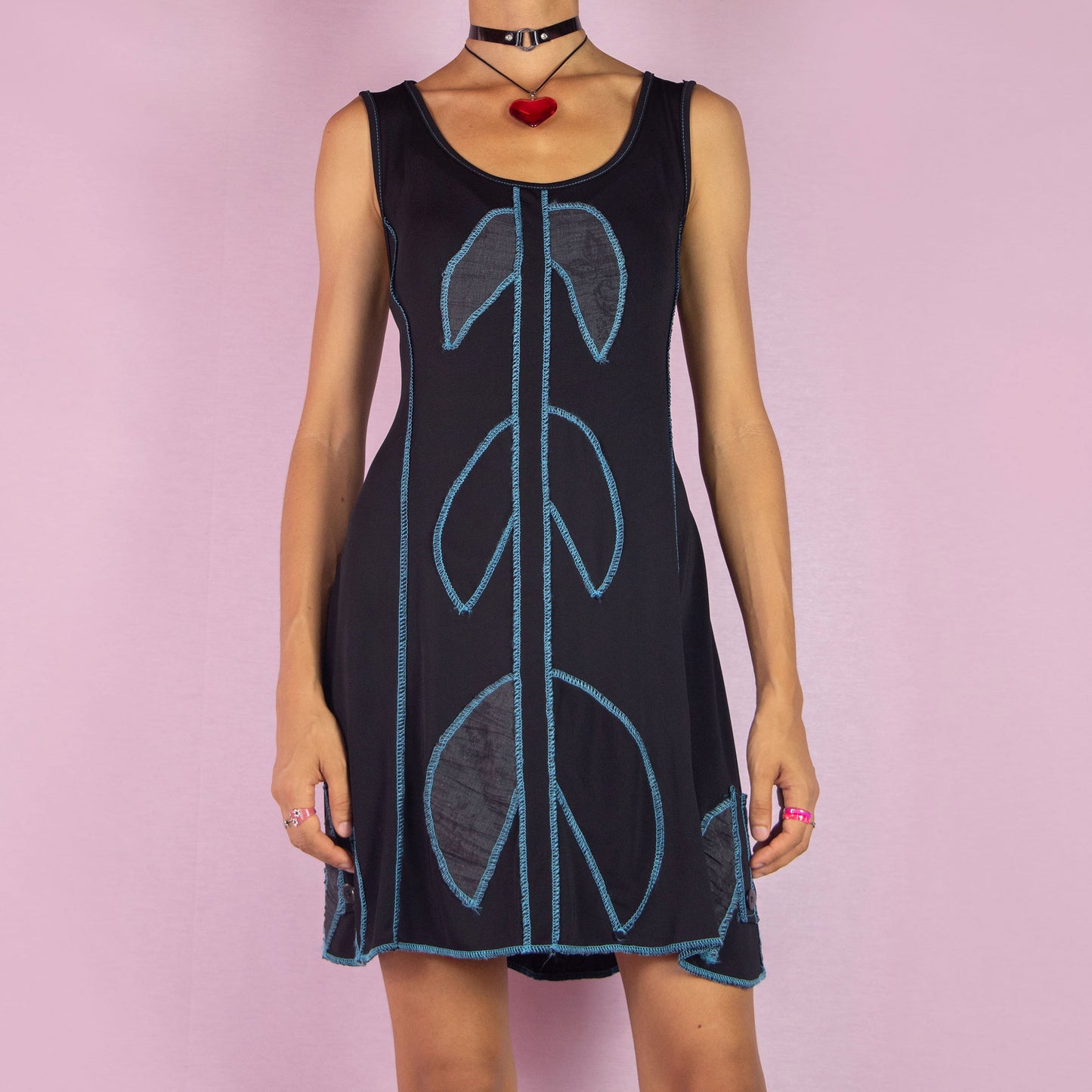 The Y2K Black Mini Sleeveless Dress is a vintage 2000s piece featuring a scoop neckline. This mini dress showcases a bold blue contrast-stitched design and is made from stretchy fabric. It includes a tie-back detail for an adjustable fit. Perfect for summer casual outings.