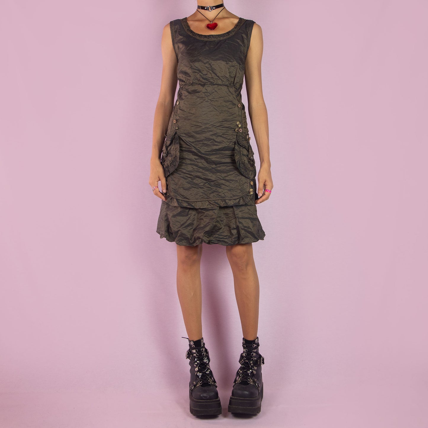 The Vintage 90s Layered Sleeveless Dress is a unique piece featuring a scoop neckline and an earthy olive-green tone. Designed with textured fabric, this dress includes a side zipper closure and detailed button accents along the sides and pockets. The layered skirt adds dimension, making it ideal for formal events or night parties.