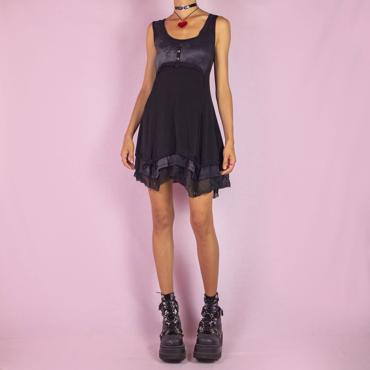 The Y2K Sleeveless Black Mini Dress is a vintage 2000s piece featuring a sleeveless design with a scoop neckline. Made from stretchy fabric, this dress has a buttoned bodice detail and a subtle tie-dye print across the top. The layered ruffle hem with mesh accents and adjustable drawstring ties adds a customizable fit. Perfect for summer casual outings or night parties.