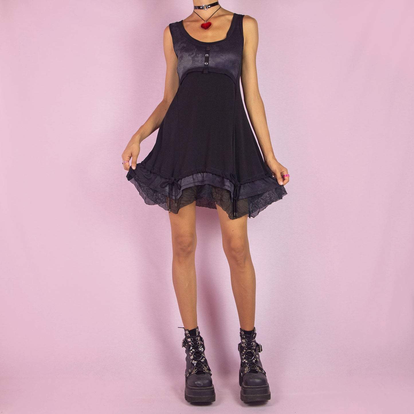 The Y2K Sleeveless Black Mini Dress is a vintage 2000s piece featuring a sleeveless design with a scoop neckline. Made from stretchy fabric, this dress has a buttoned bodice detail and a subtle tie-dye print across the top. The layered ruffle hem with mesh accents and adjustable drawstring ties adds a customizable fit. Perfect for summer casual outings or night parties.